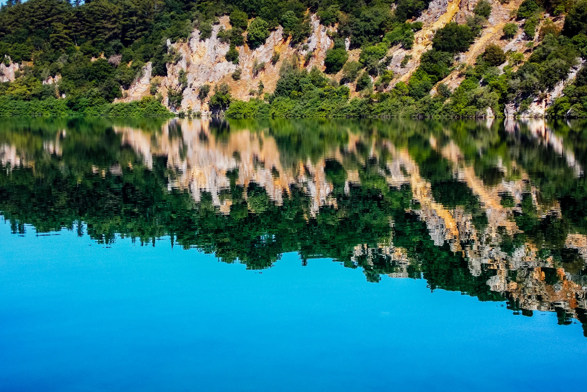 Rocky forest shoreline mirrored in the still surface of a lake