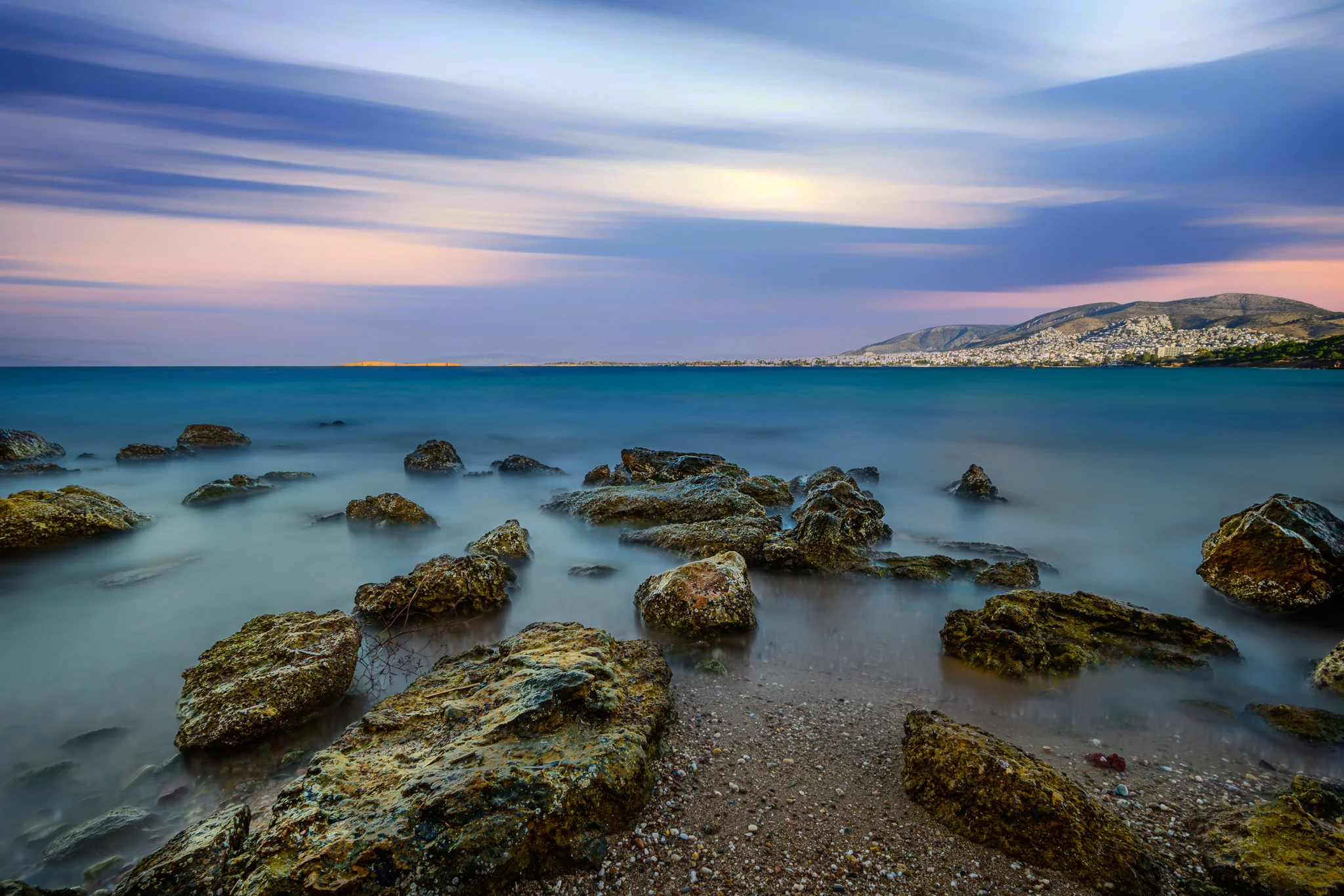Rocky shoreline and softened sea facing a distant hillside coastal town