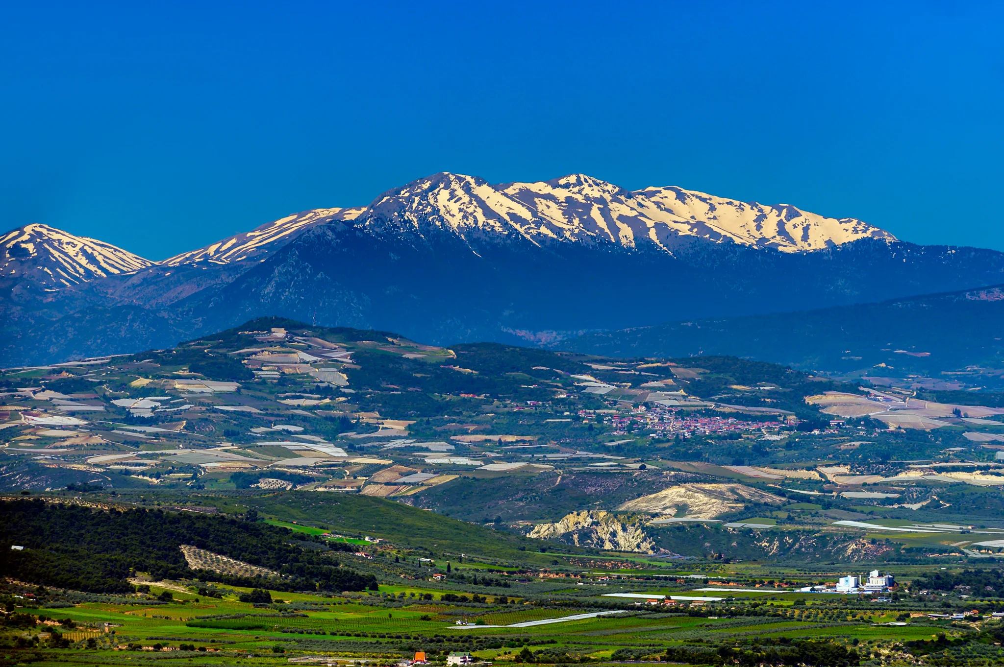 Snow-streaked mountain range above a cultivated valley and village
