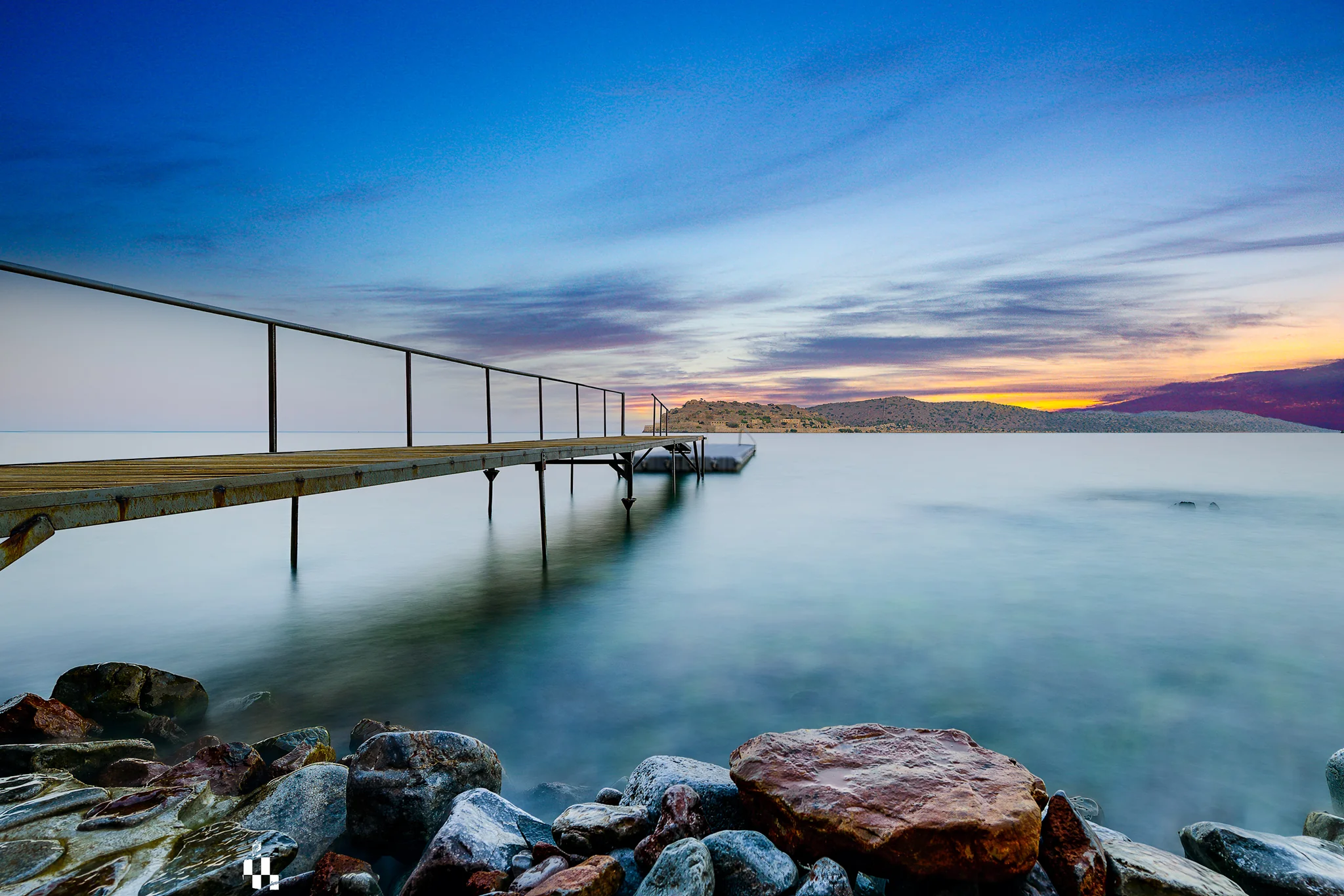 Narrow metal pier extending over a rocky coast at sunset