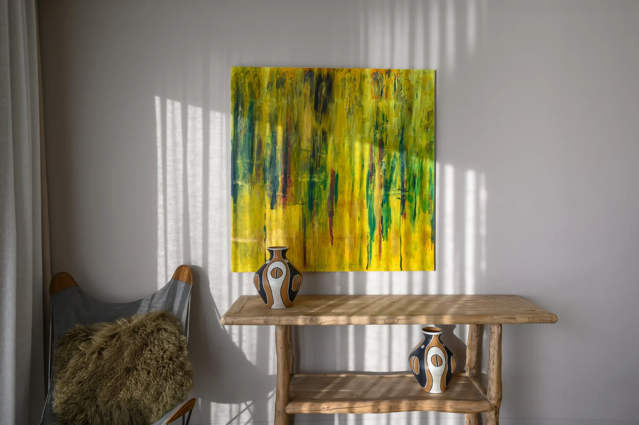 Yellow abstract painting above a timber console with patterned ceramic vases, beside a butterfly chair and bands of sunlight on the wall at The Olive Retreat near Pylos.