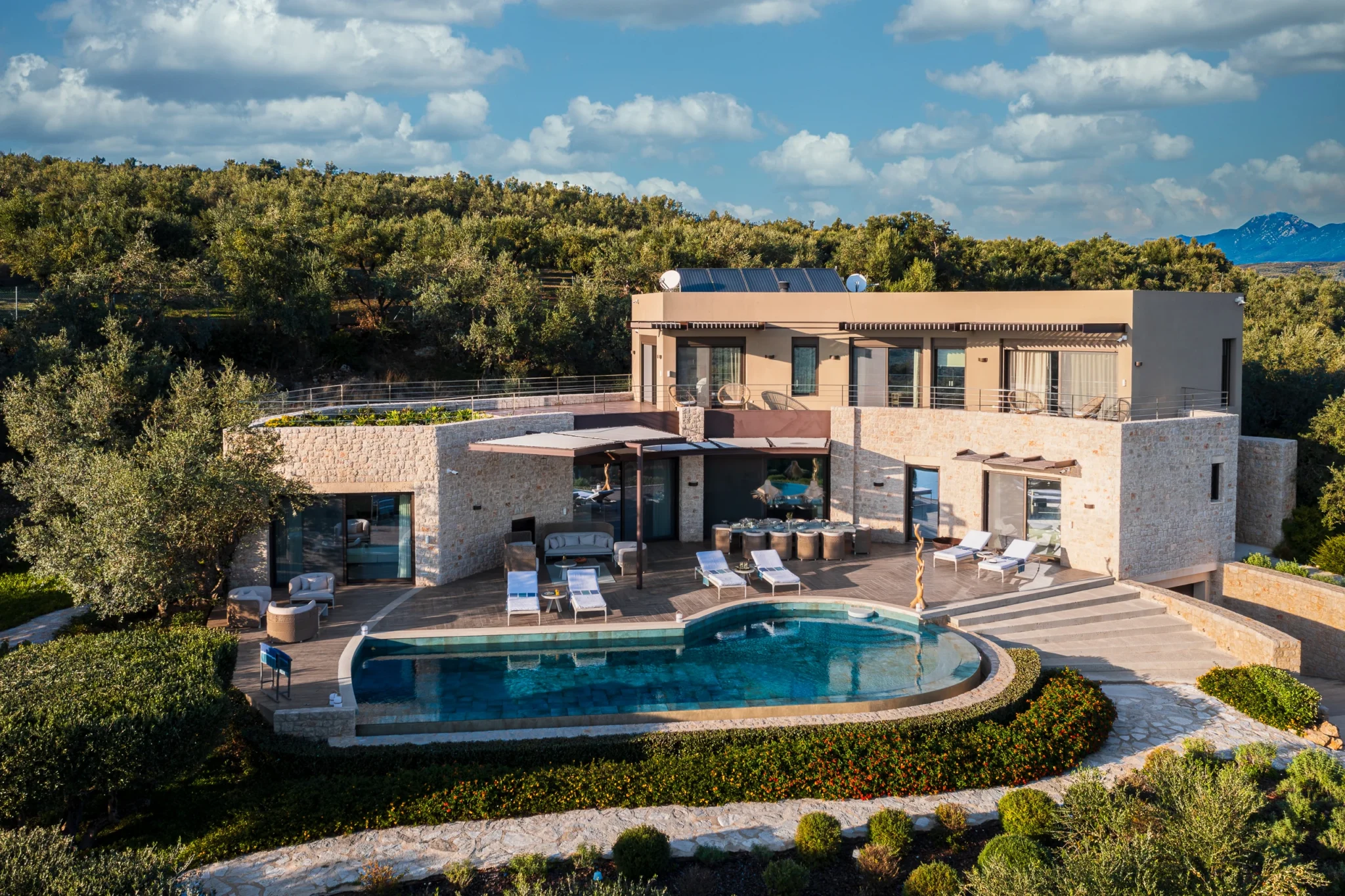 Elevated view of the stone retreat, curved swimming pool, sun loungers and terraces surrounded by an extensive olive grove at The Olive Retreat near Pylos.