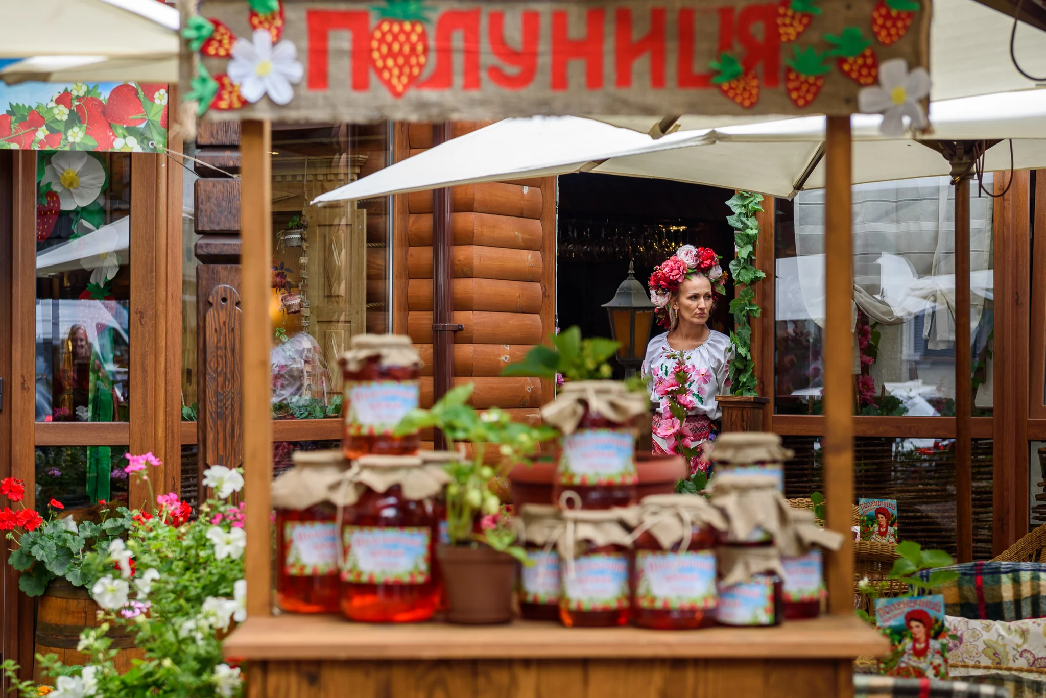 Woman in traditional floral dress at a market stall displaying preserves
