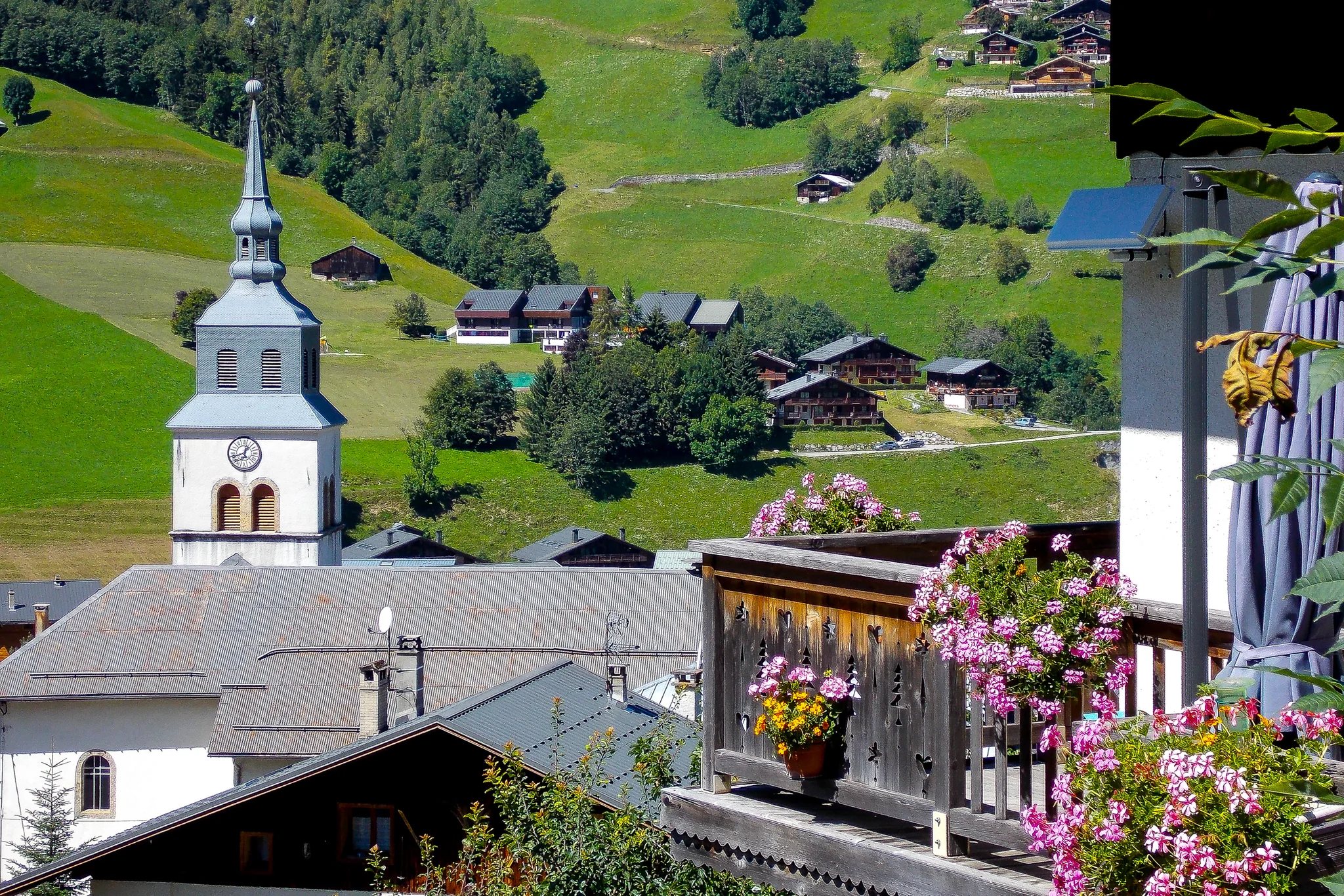 White church tower and flowered balconies in a green alpine village