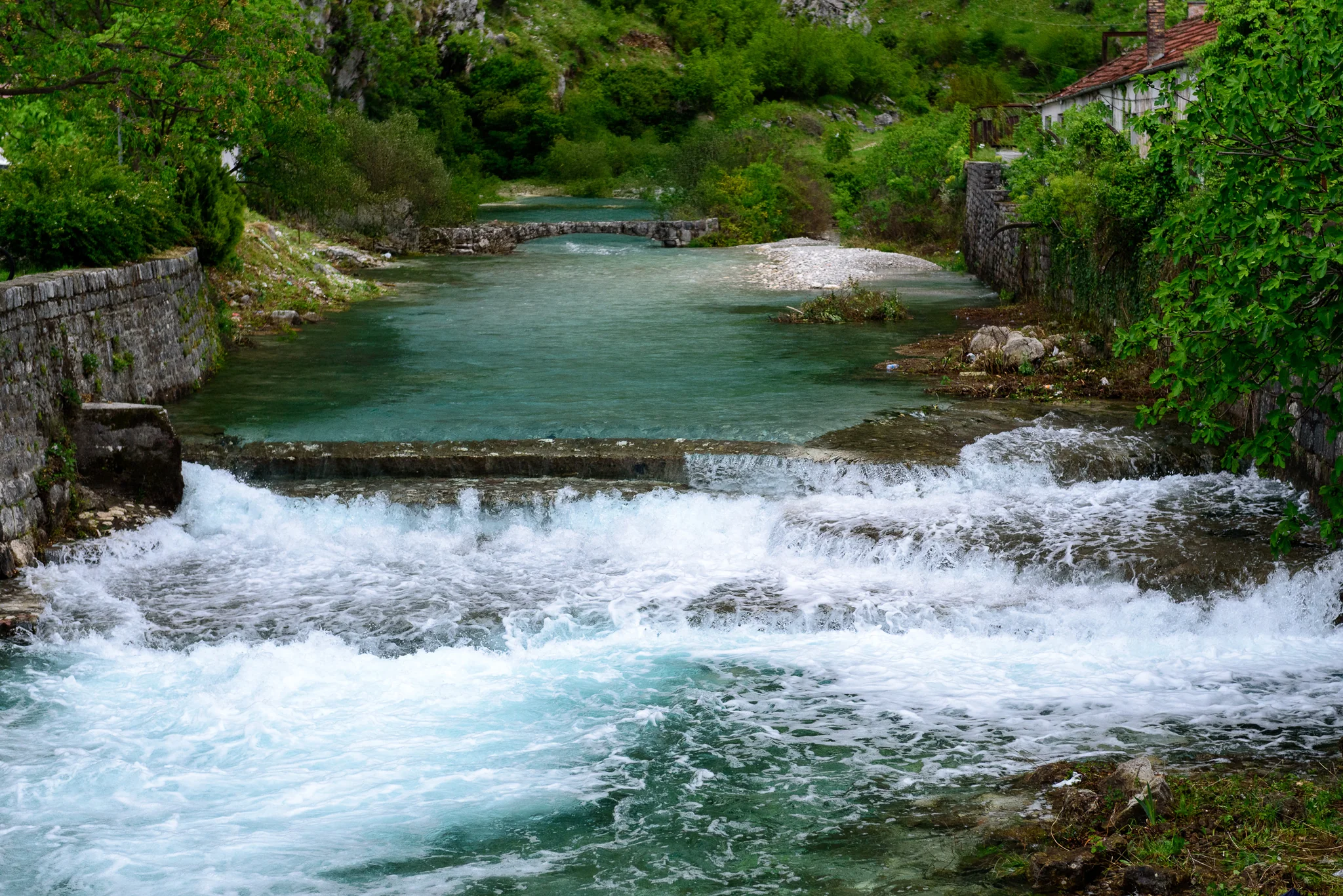 Clear mountain river flowing past a low stone bank and green hillside