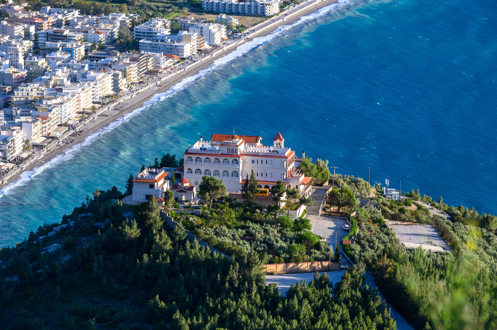 Elevated view of a monastery complex above a long urban coastline