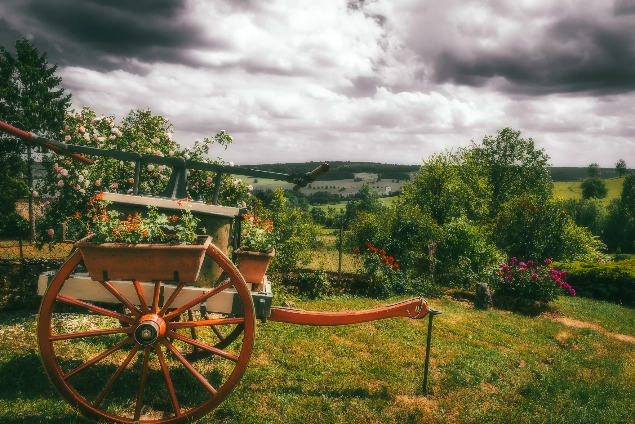 Traditional wooden cart in a rural garden beneath dark storm clouds