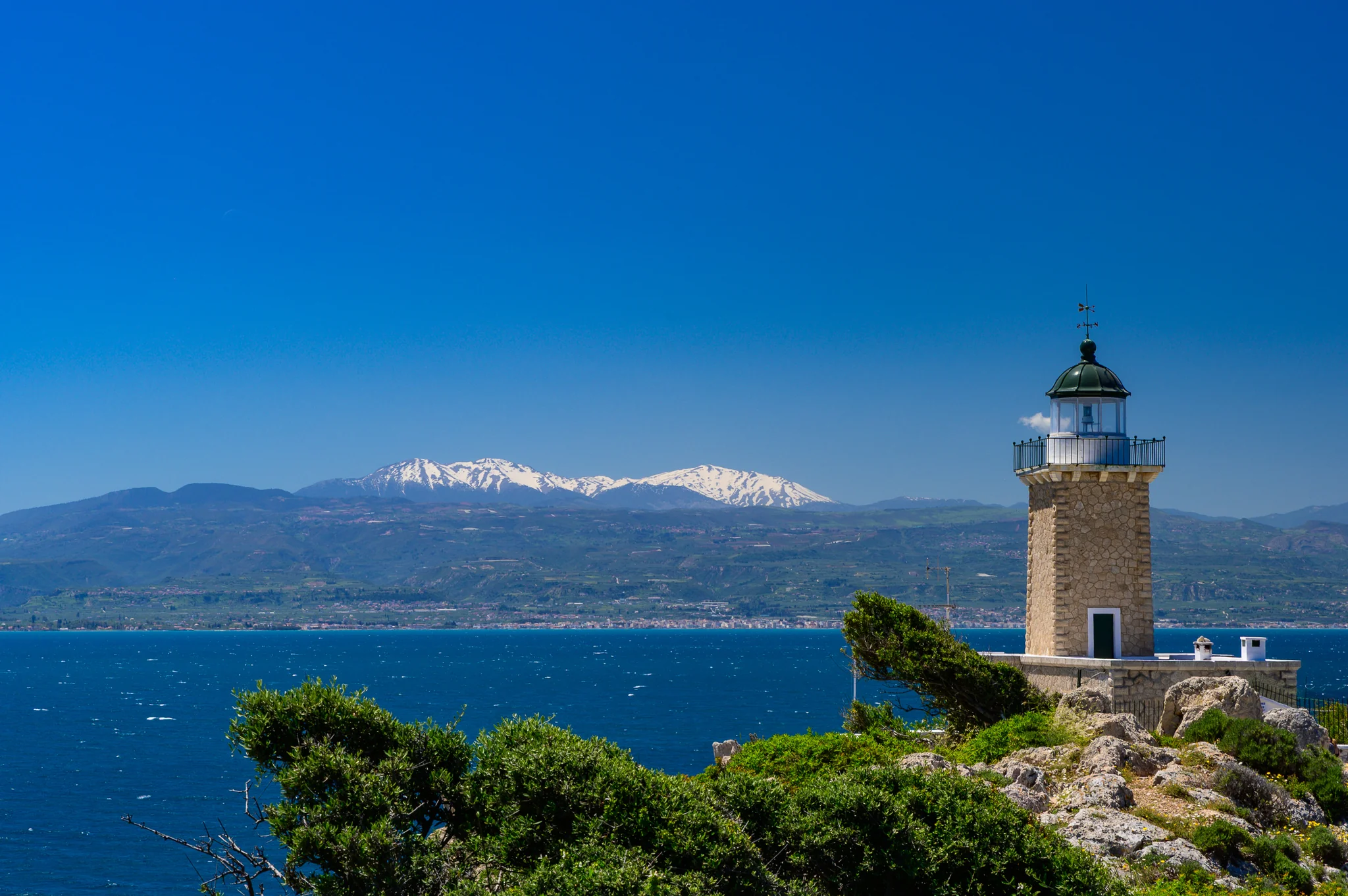 Stone lighthouse on a wooded headland overlooking deep blue water