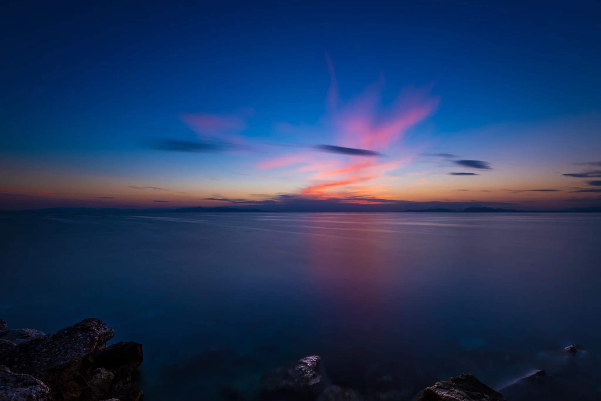 Long-exposure seascape with a small rock beneath pink twilight clouds