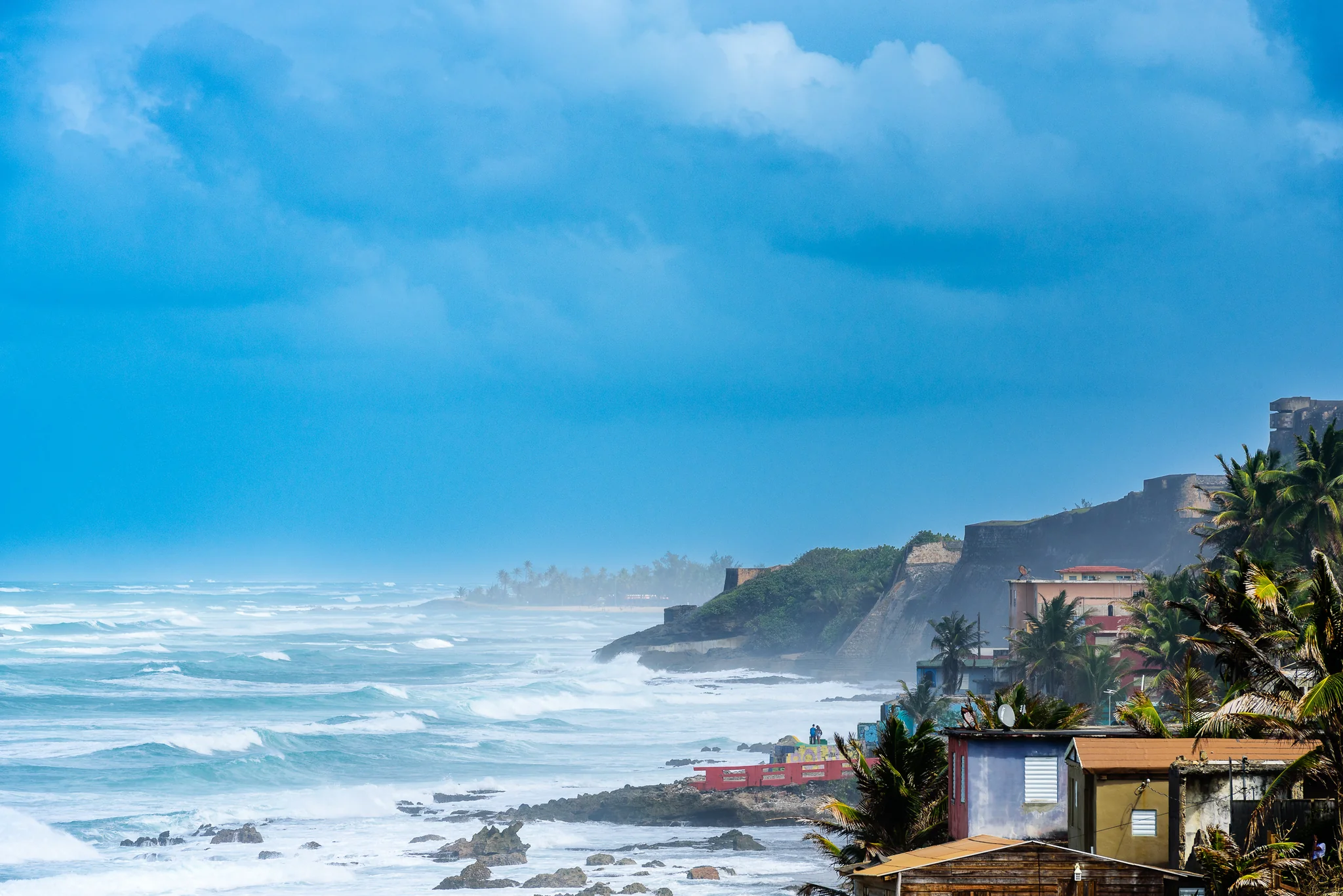 Powerful surf breaking along a developed coast beneath dark cliffs