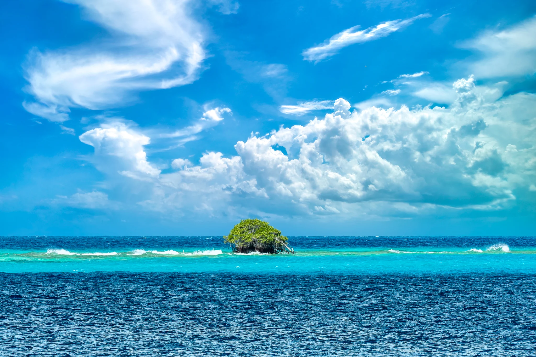 Small green tropical islet surrounded by turquoise and deep blue water