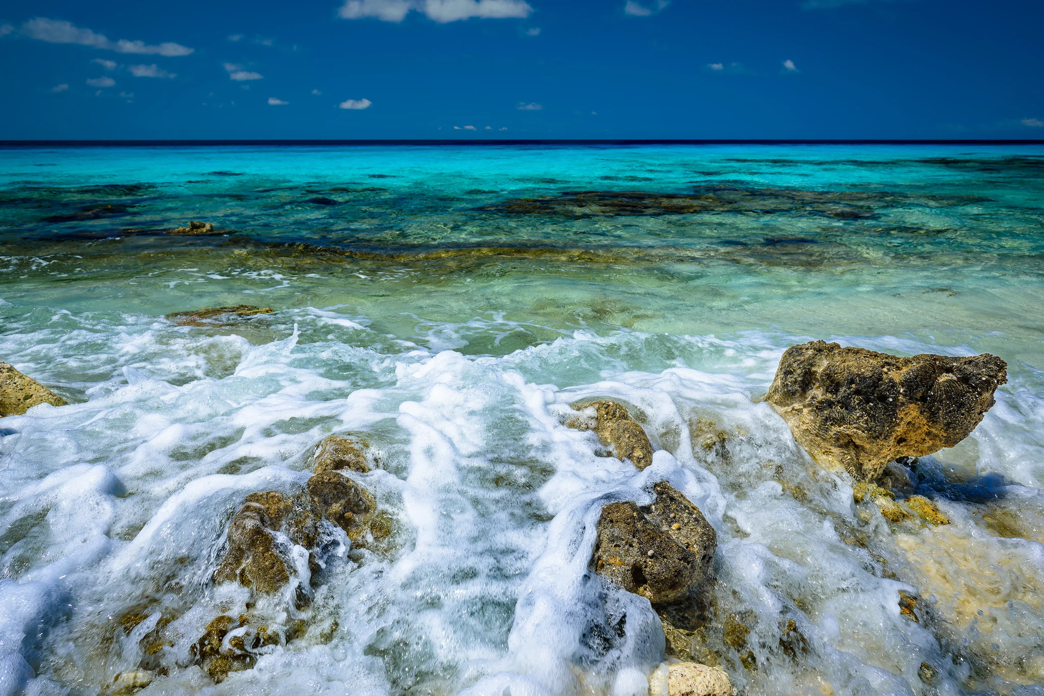 Turquoise waves breaking across rocks beneath a bright blue sky