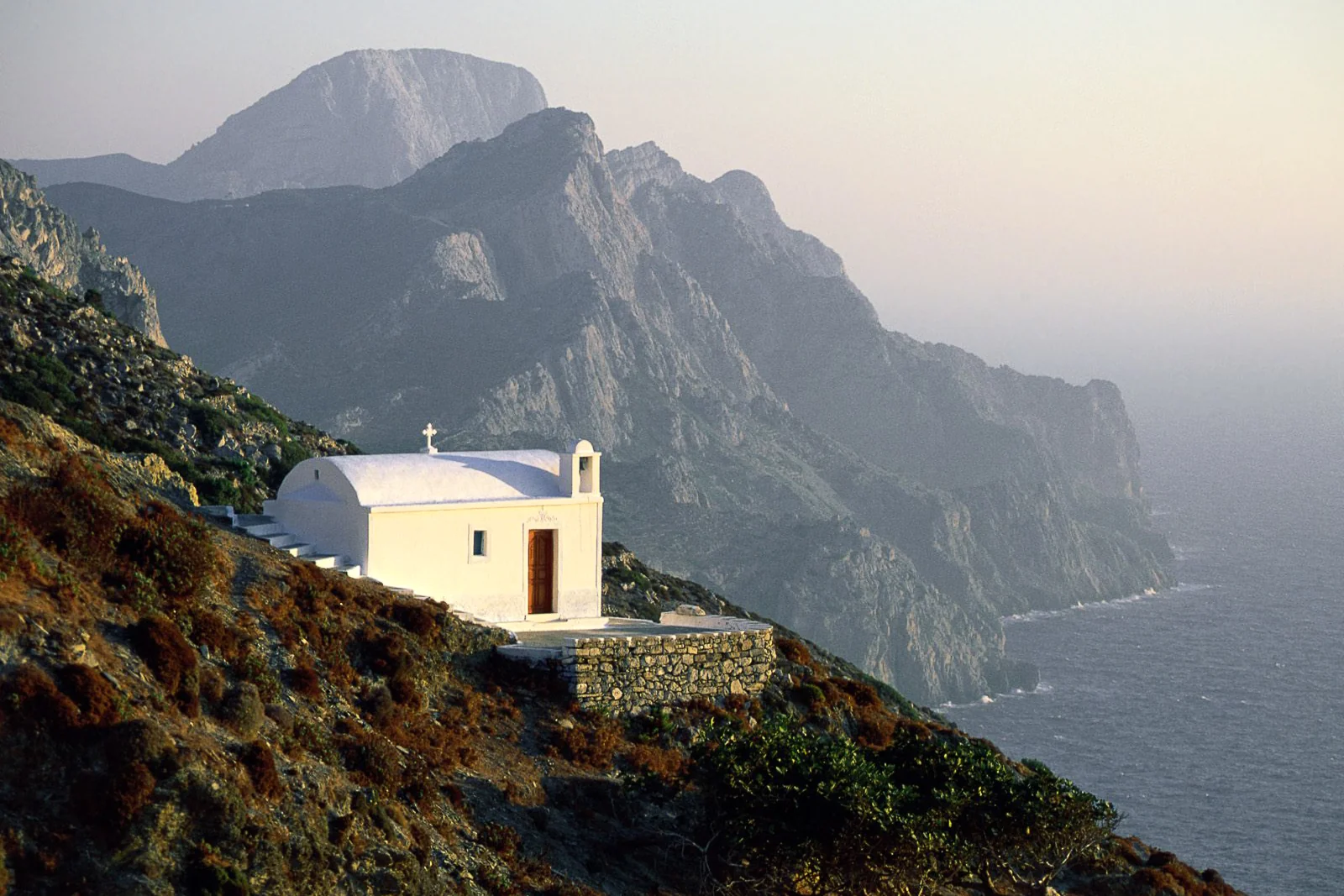 Small white chapel on a steep mountainside above the sea