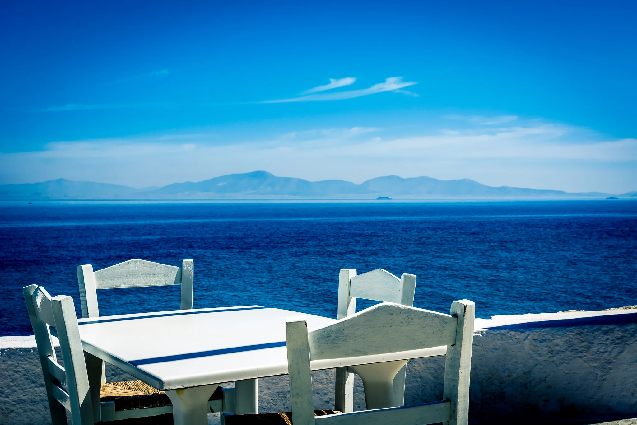 White table and chairs on a terrace overlooking deep blue water