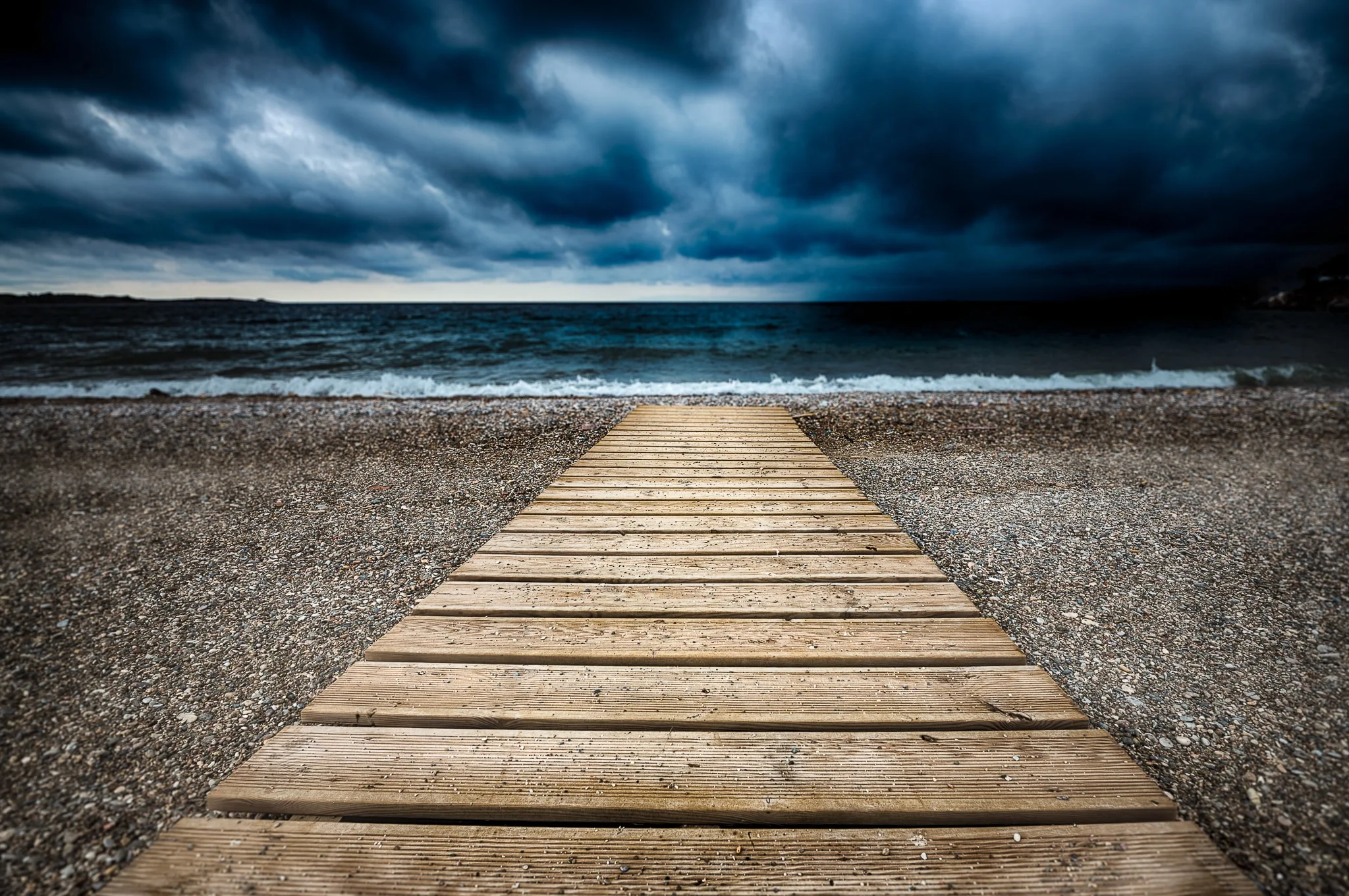 Wooden pier extending toward dark water beneath storm clouds