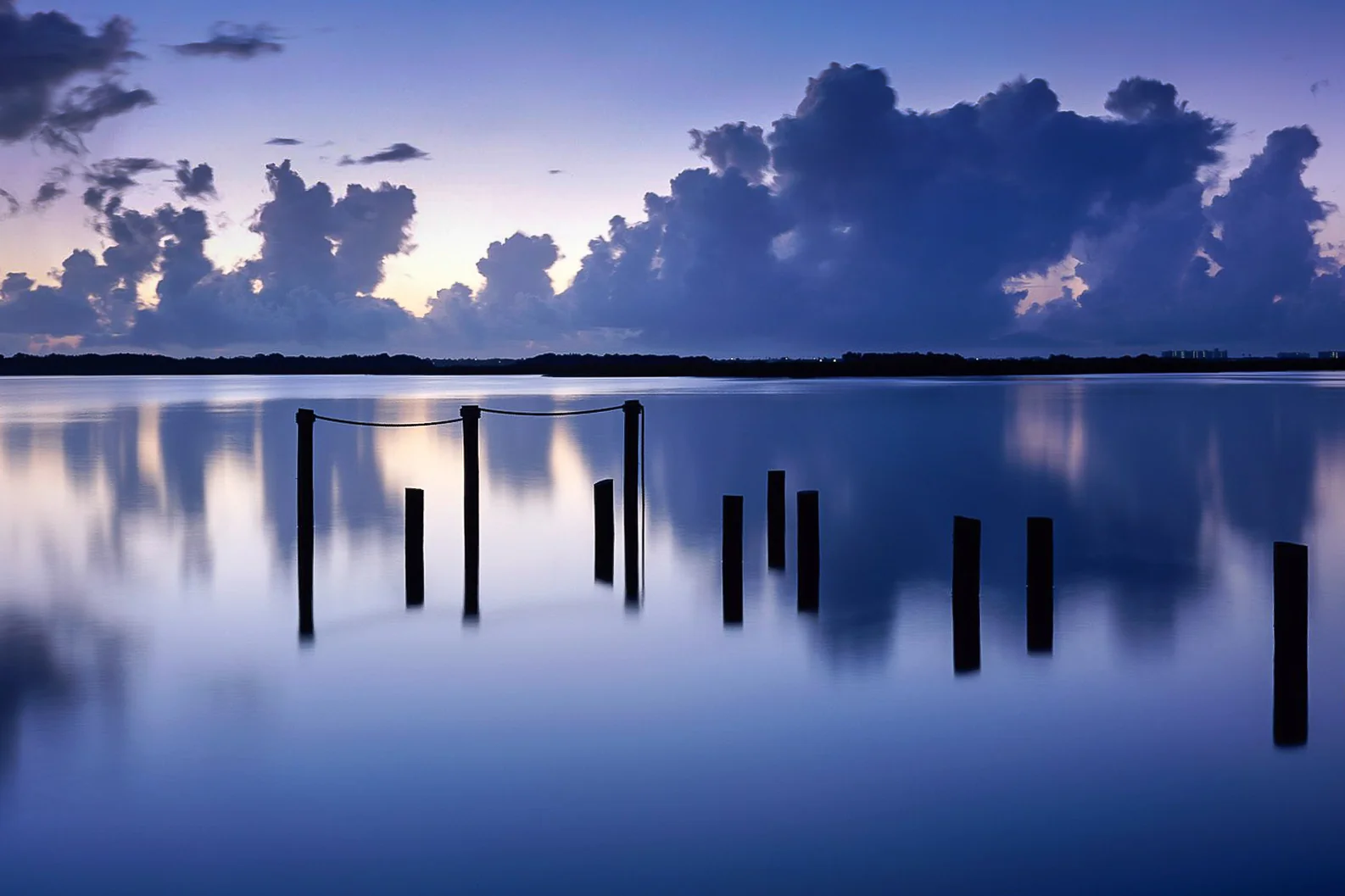 Rows of wooden posts reflected in a still lake beneath purple clouds