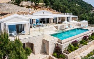 Aerial view of Villa Artemis with a turquoise pool, pale facade and stone terraces in Corfu, Greece