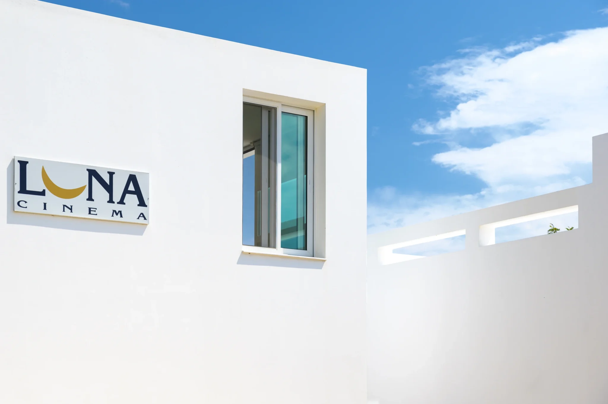 Luna Cinema sign beside a tall window on a white facade, with horizontal terrace openings against a blue sky at Villa Bel Air in Porto Heli.
