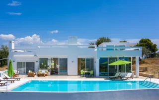 White villa with broad glazed openings, lime-green parasols and sun loungers overlooking a turquoise swimming pool at Villa Bel Air in Porto Heli.
