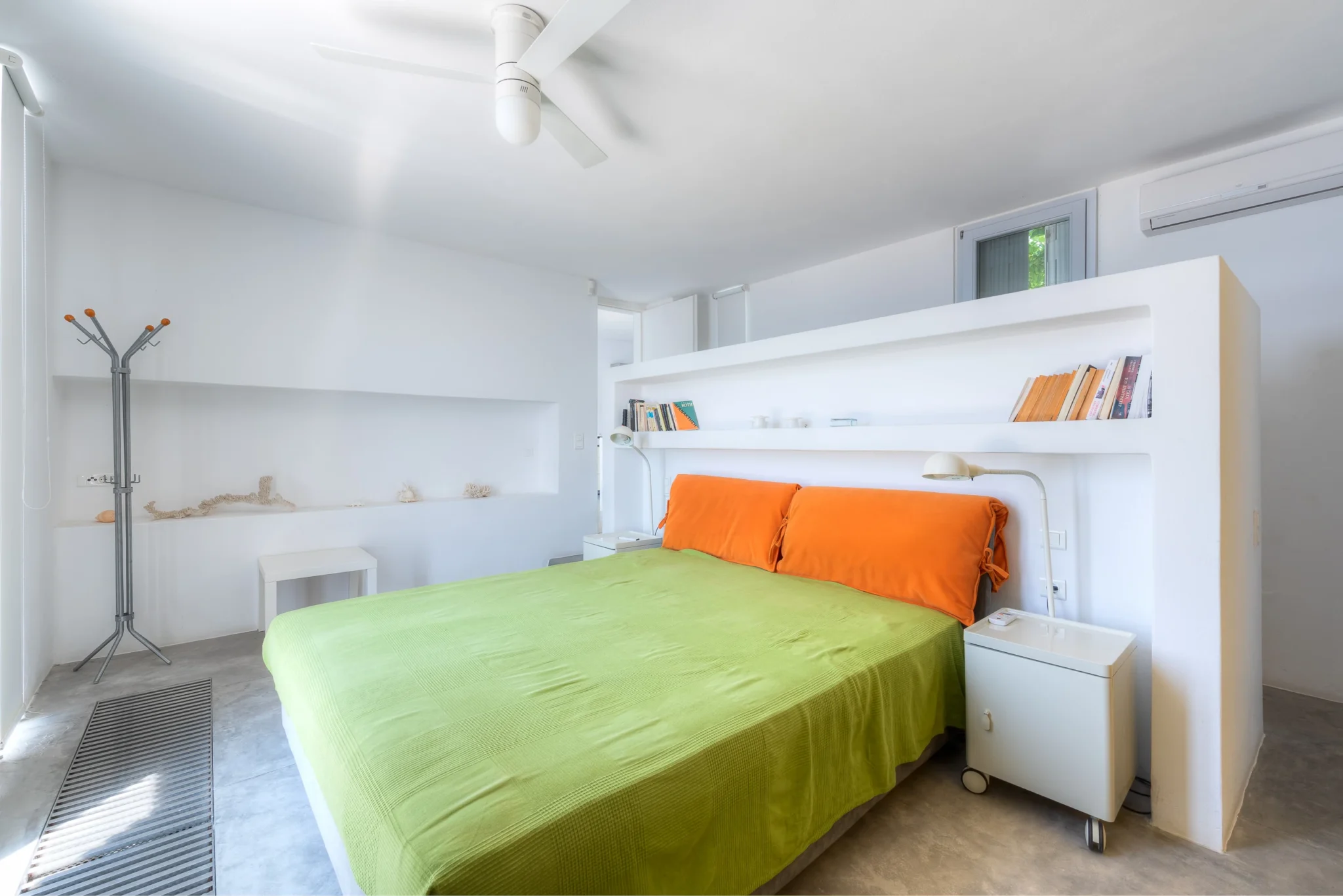White bedroom with a lime green bedcover, orange head cushions and built-in shelving at Villa Edge in Paros.