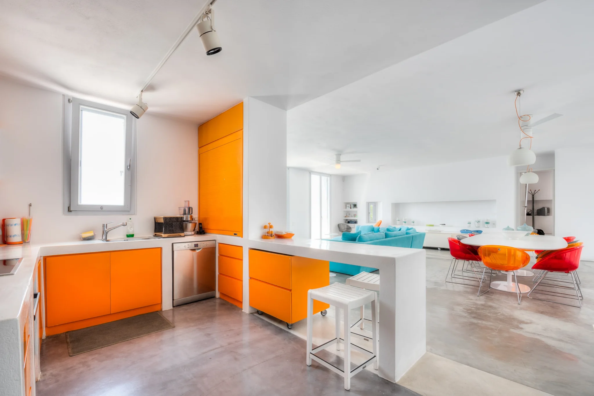 Orange kitchen cabinetry and a white breakfast counter connect to the living and dining areas at Villa Edge in Paros.