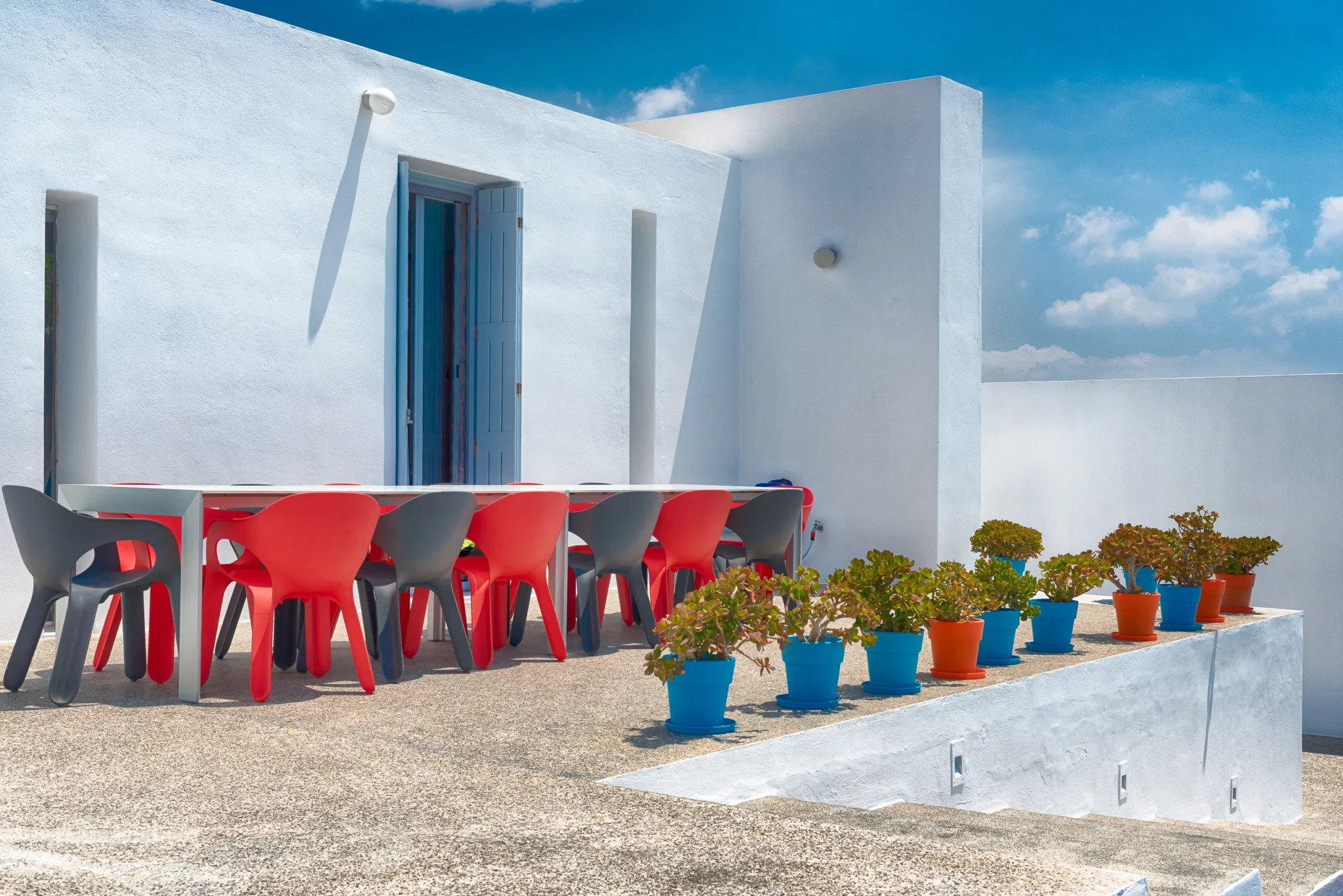 Red and grey chairs around an outdoor dining table beside turquoise and orange plant pots at Villa Edge in Paros.