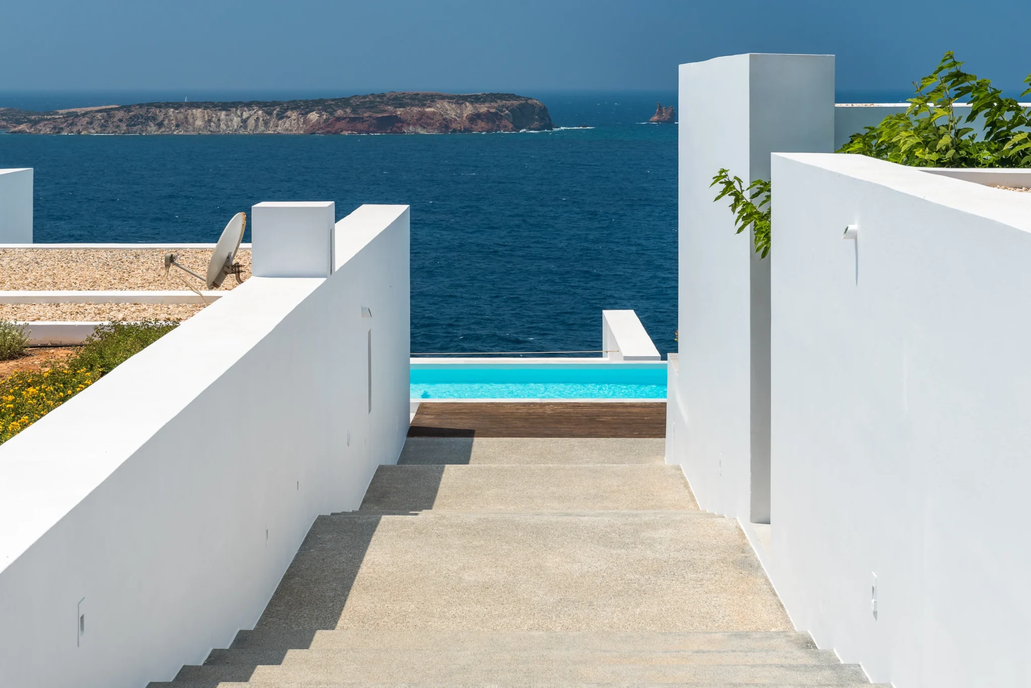 Steps between white walls lead towards the swimming pool and an Aegean sea view at Villa Edge in Paros.
