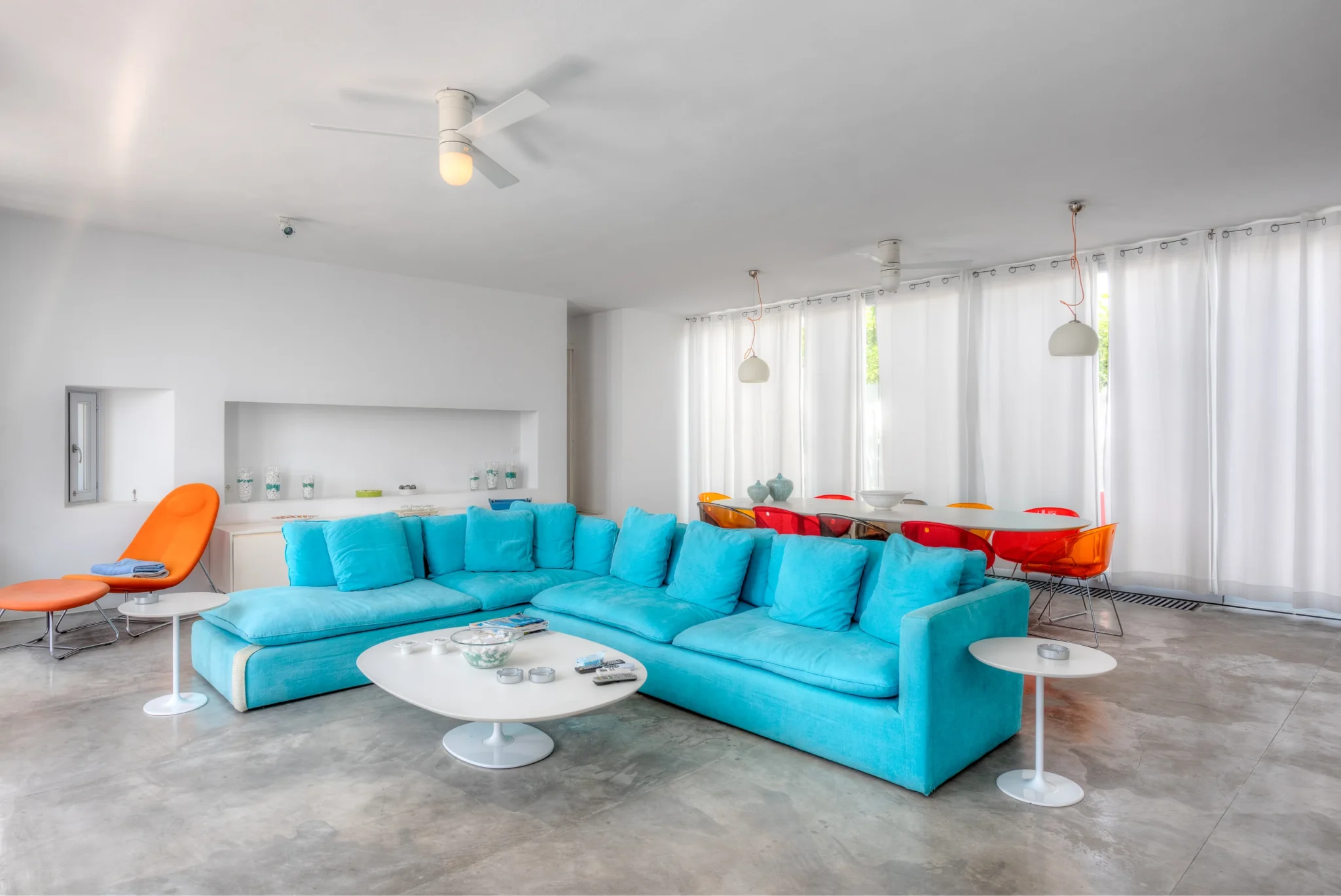 Turquoise corner sofa, orange lounge chair and colourful dining chairs in the bright white interior of Villa Edge in Paros.