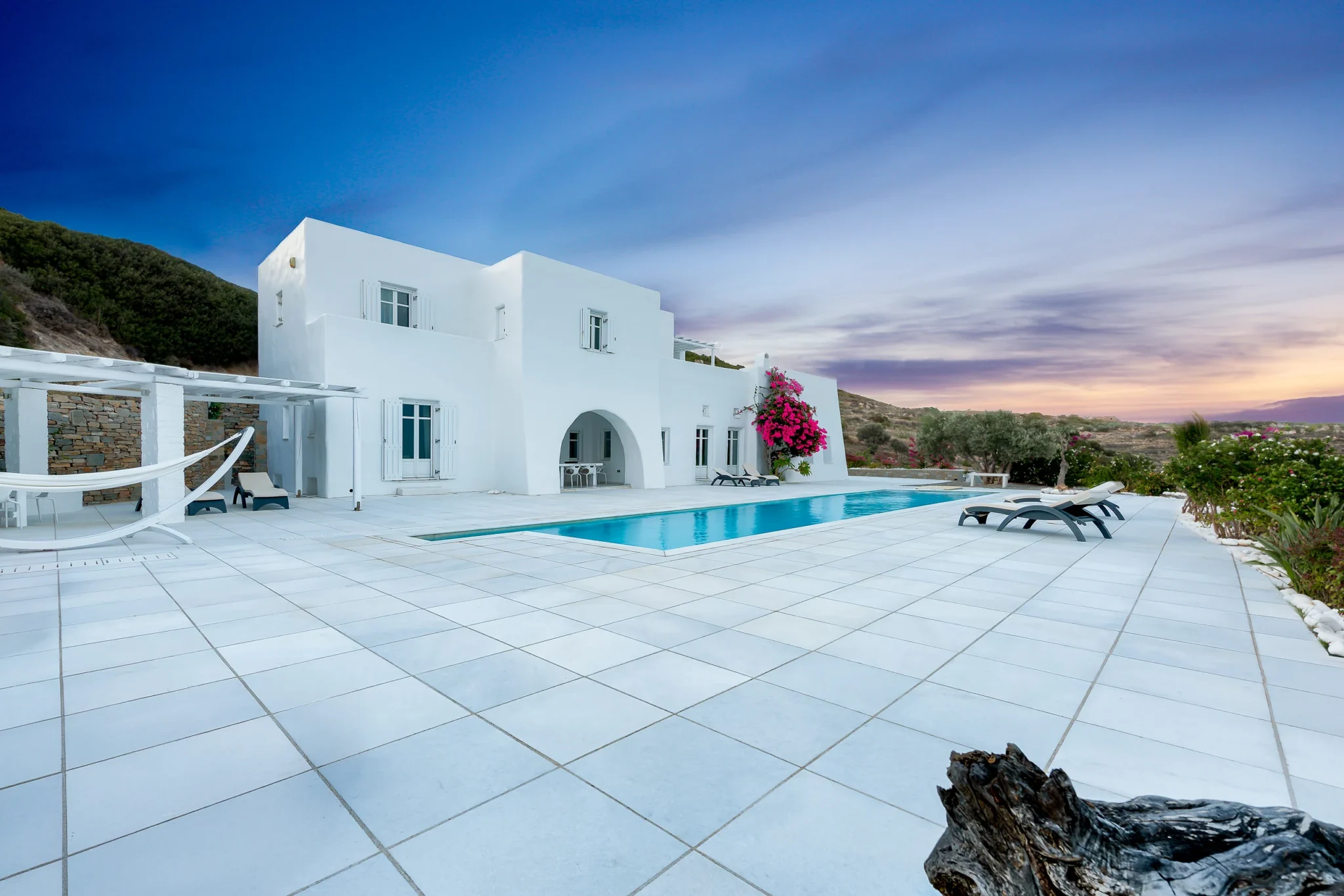 White villa and swimming pool beneath a pink and blue twilight sky at Villa Full Moon in Paros, Greece.