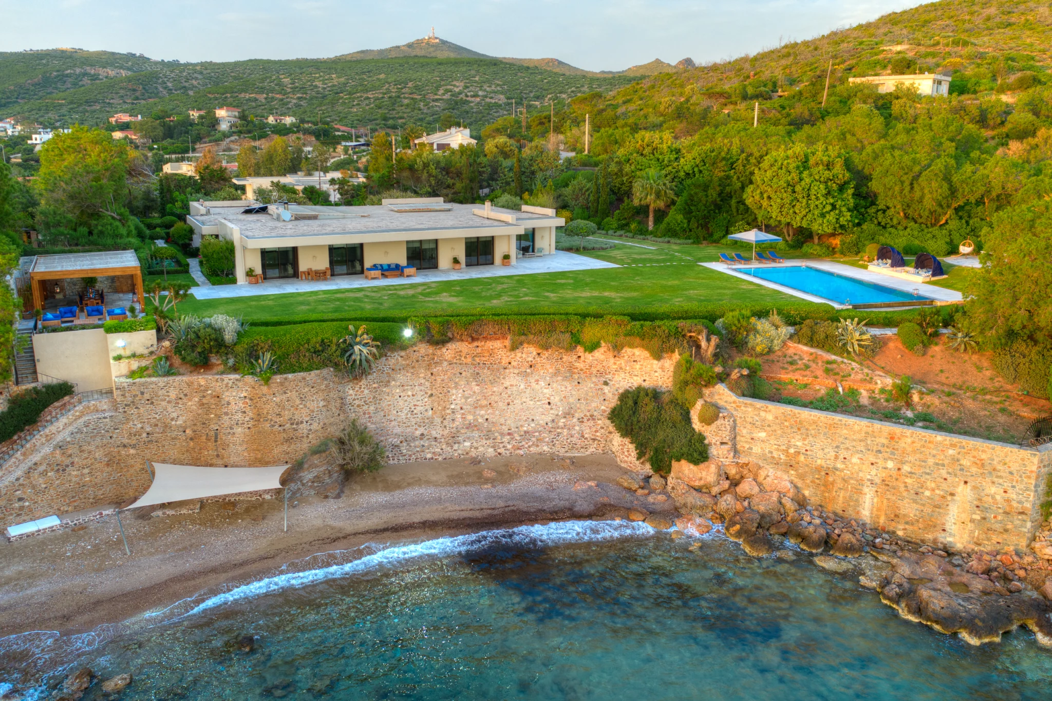 Aerial view of the villa, its gardens and swimming pool above a rocky shoreline at Villa Icarus.