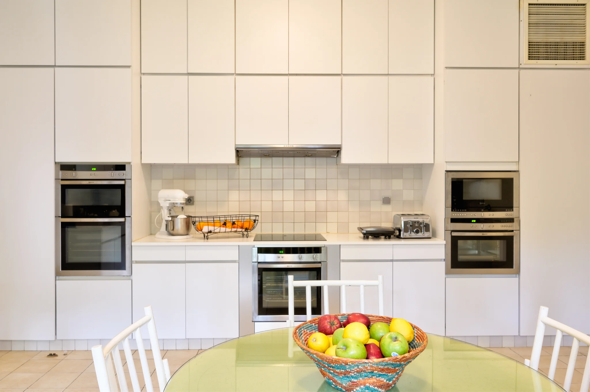 White kitchen with built-in ovens and a fruit bowl on the breakfast table at Villa Icarus.