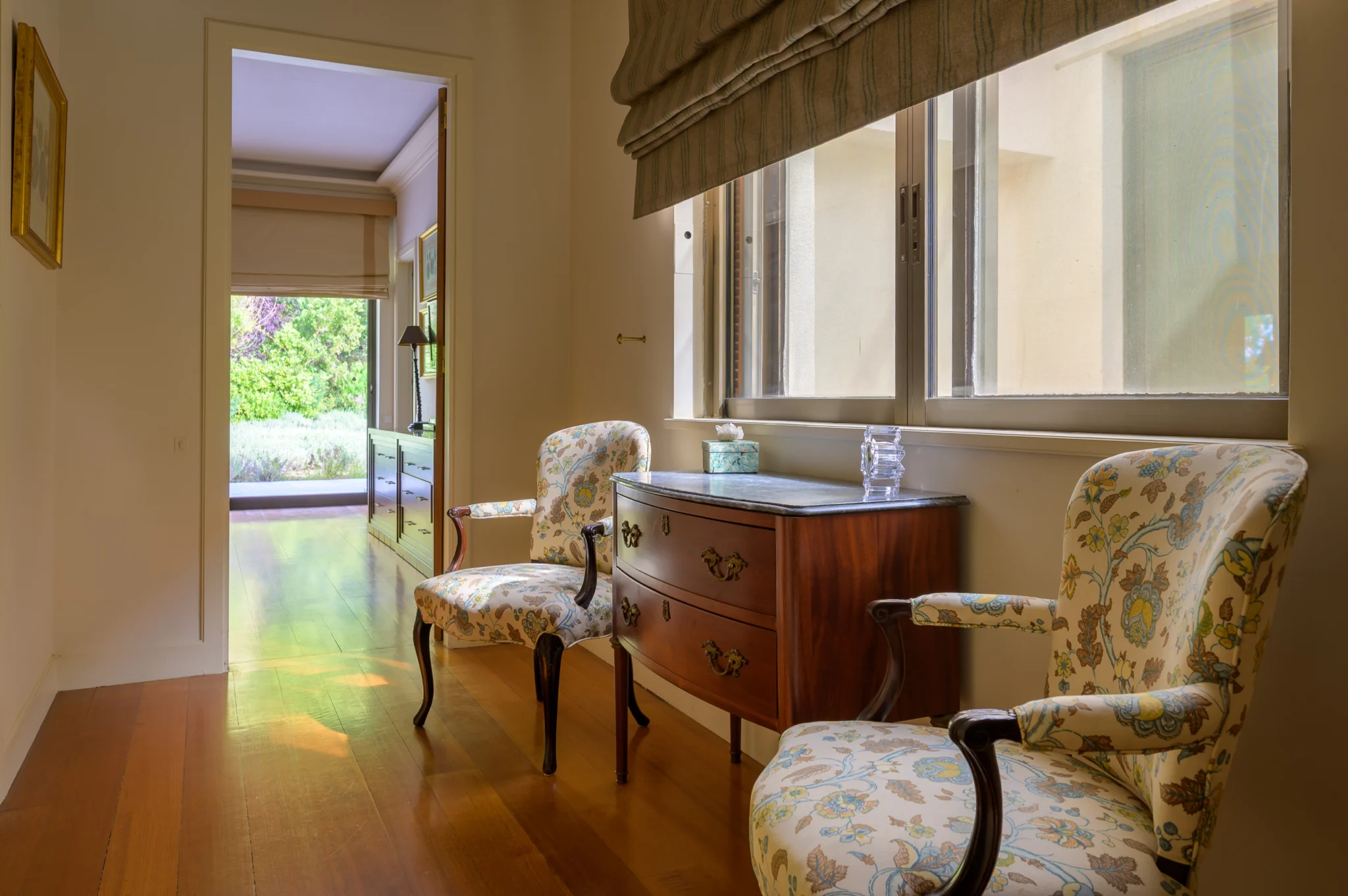 Floral armchairs and a chest of drawers beside a bedroom window at Villa Icarus.