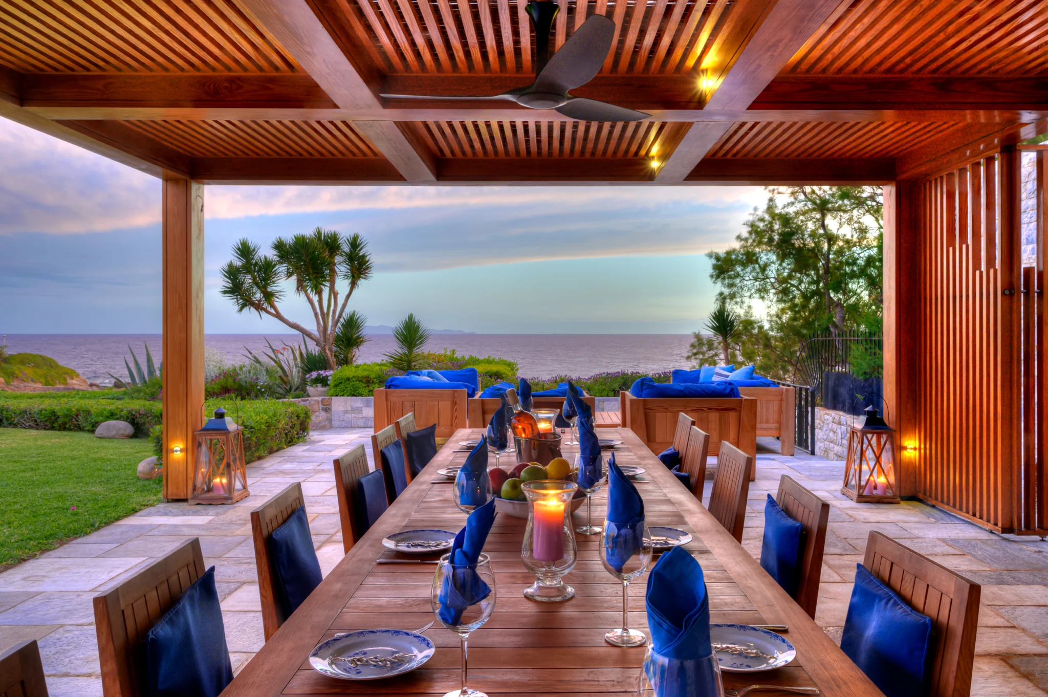 Outdoor dining table under a timber pergola with a sea view at sunset at Villa Icarus.
