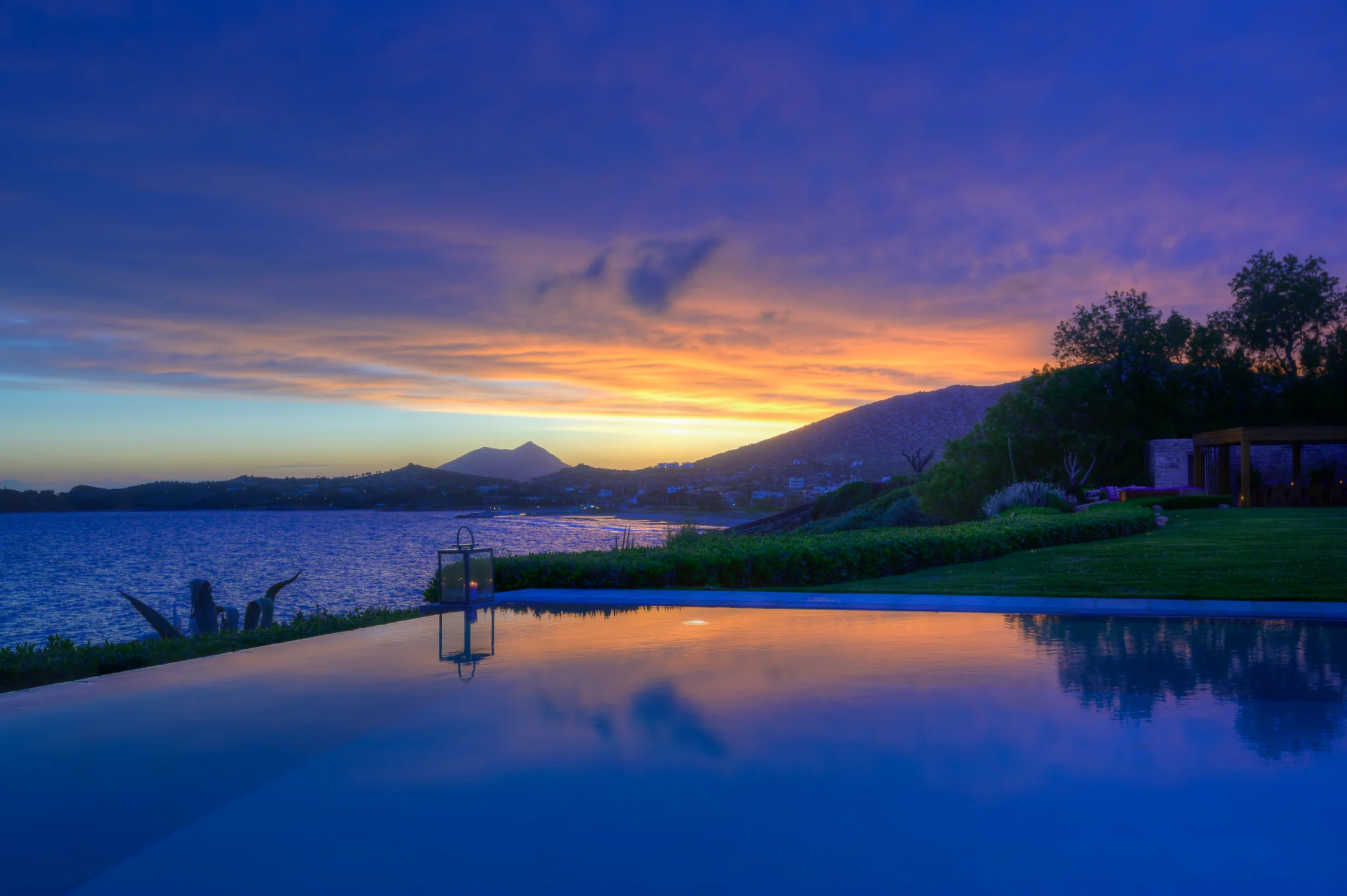 Swimming pool and coastline beneath a colourful sunset sky at Villa Icarus.
