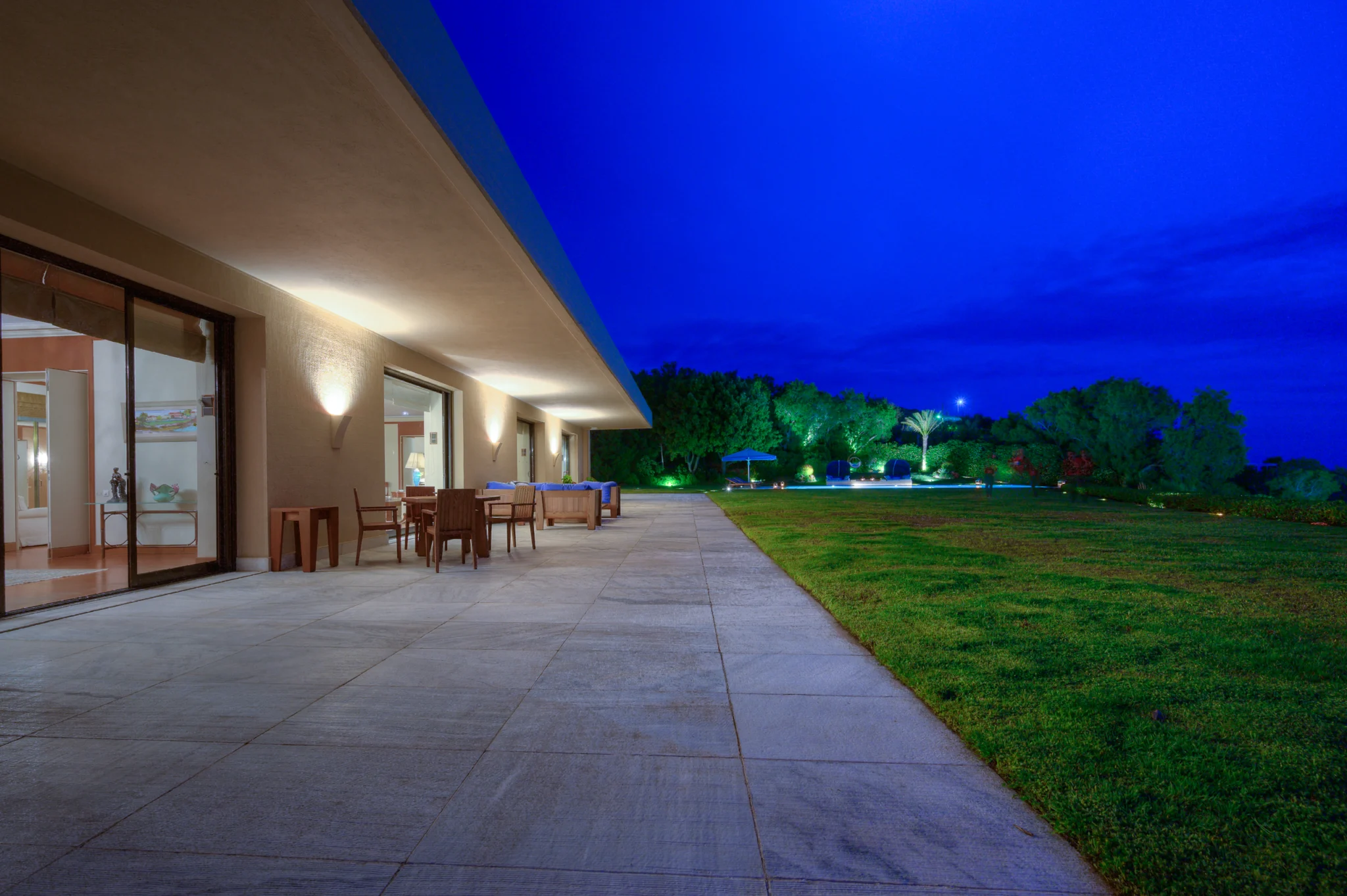 Covered terrace, outdoor dining and lawn at night at Villa Icarus.