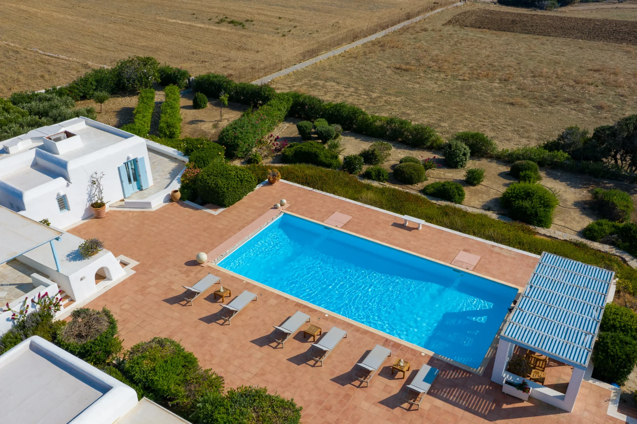 Aerial view of the rectangular swimming pool, terracotta terrace, sun loungers and pale blue pergola at Villa Lumina in Paros.