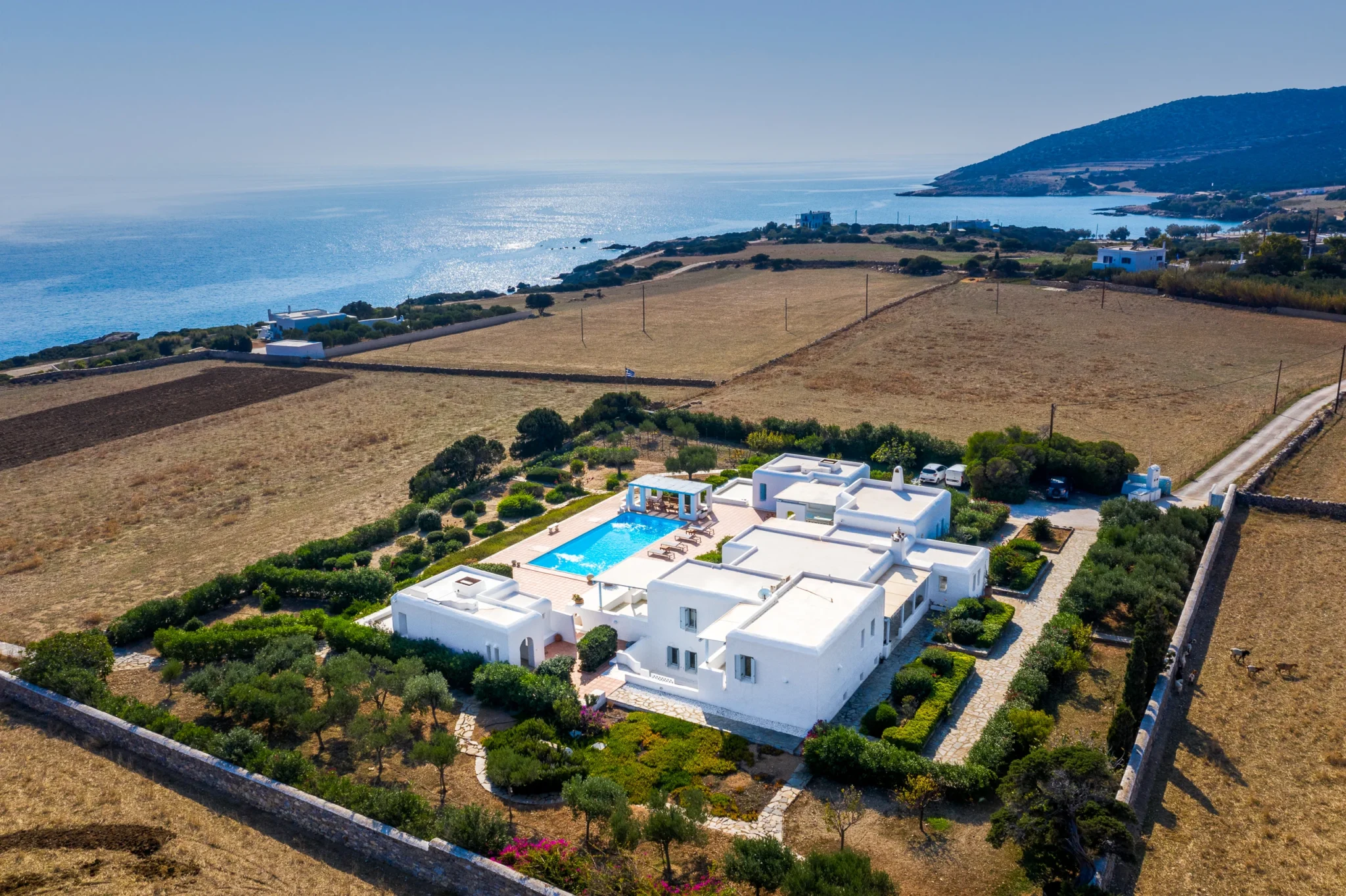 Aerial view of Villa Lumina in Paros showing the white buildings, pool and gardens within a rural landscape near the coast.