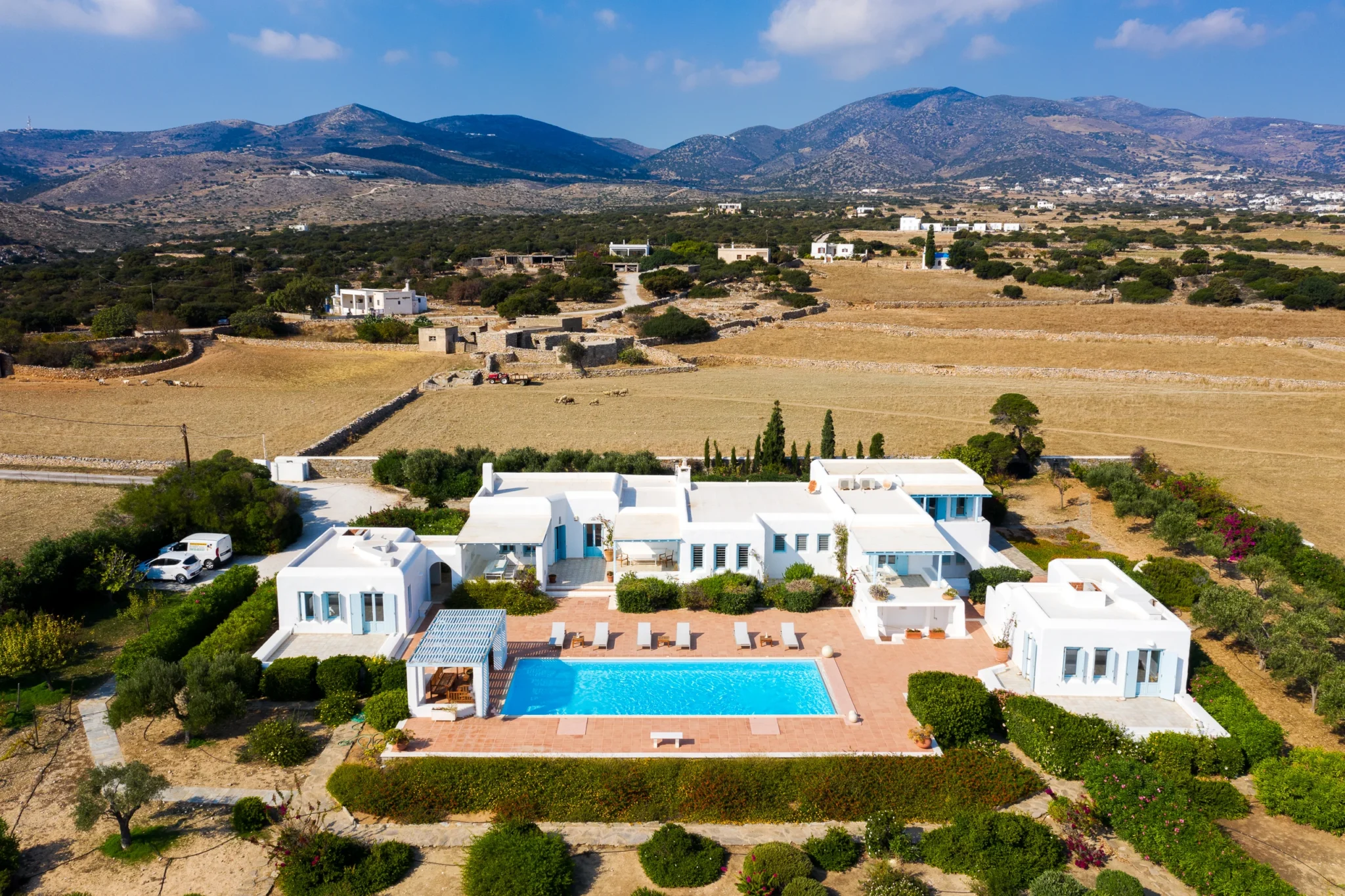 Aerial view across the pool and gardens towards Villa Lumina, surrounding fields, stone walls and the hills of Paros.