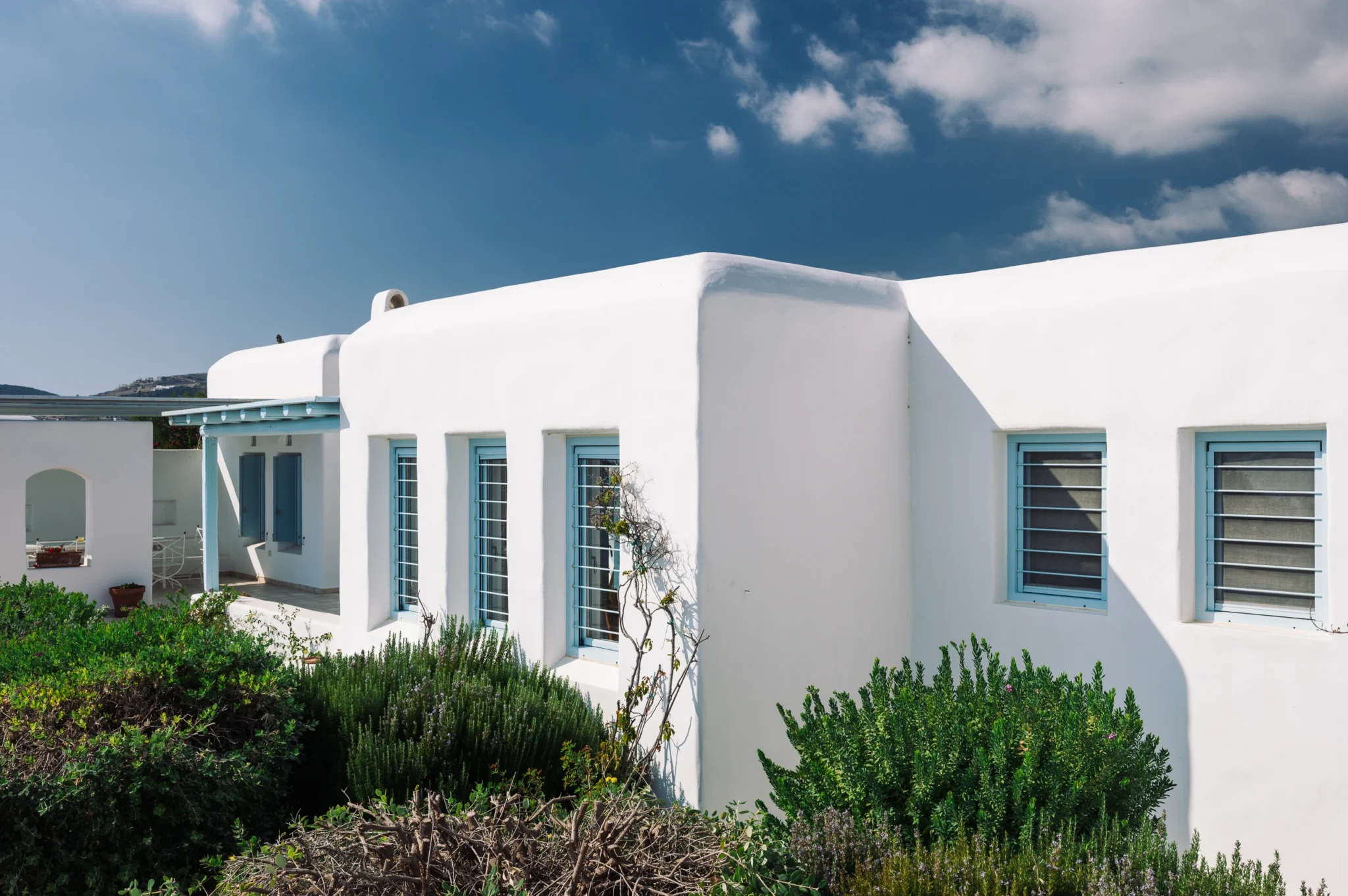 Rounded white building forms, pale blue windows and planted garden borders at Villa Lumina in Paros.
