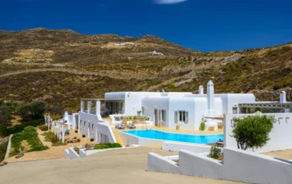 White Cycladic buildings and a turquoise swimming pool set into the rocky hillside at Villa Mariposa in Mykonos.