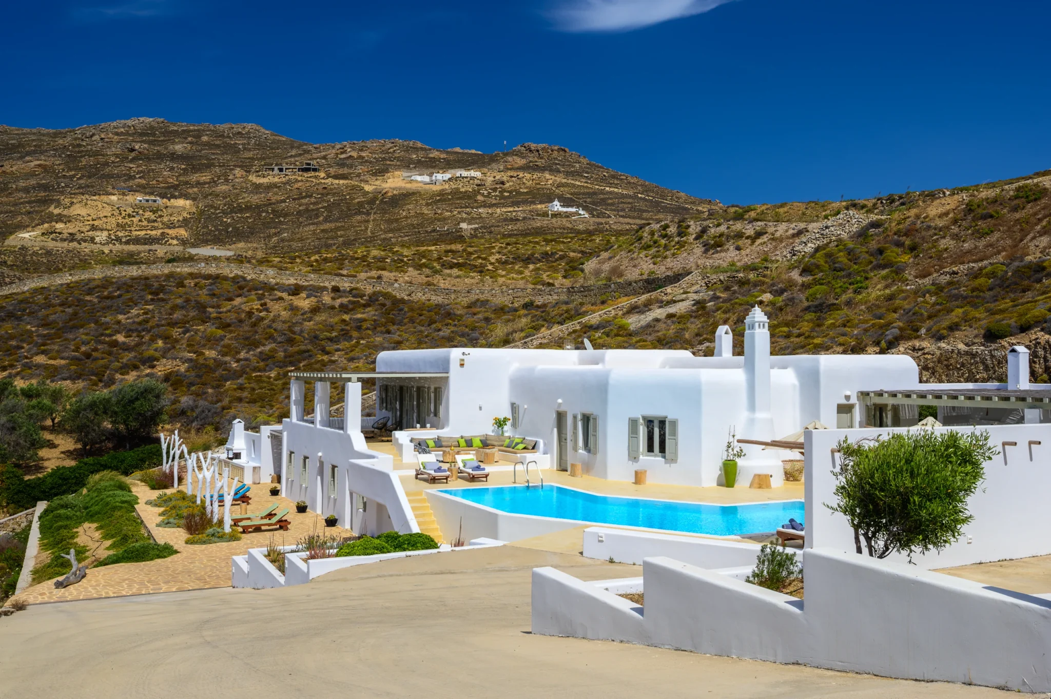 White Cycladic buildings and a turquoise swimming pool set into the rocky hillside at Villa Mariposa in Mykonos.
