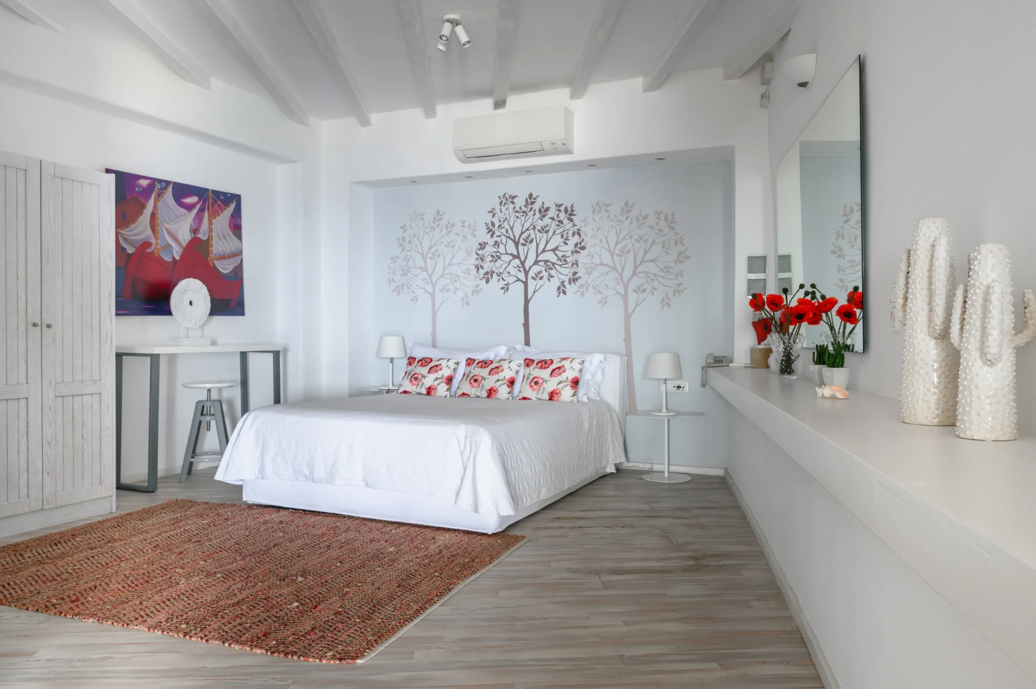 White bedroom with a tree mural, red floral cushions, a textured red rug and decorative white ceramics at Villa Mustique in Mykonos.