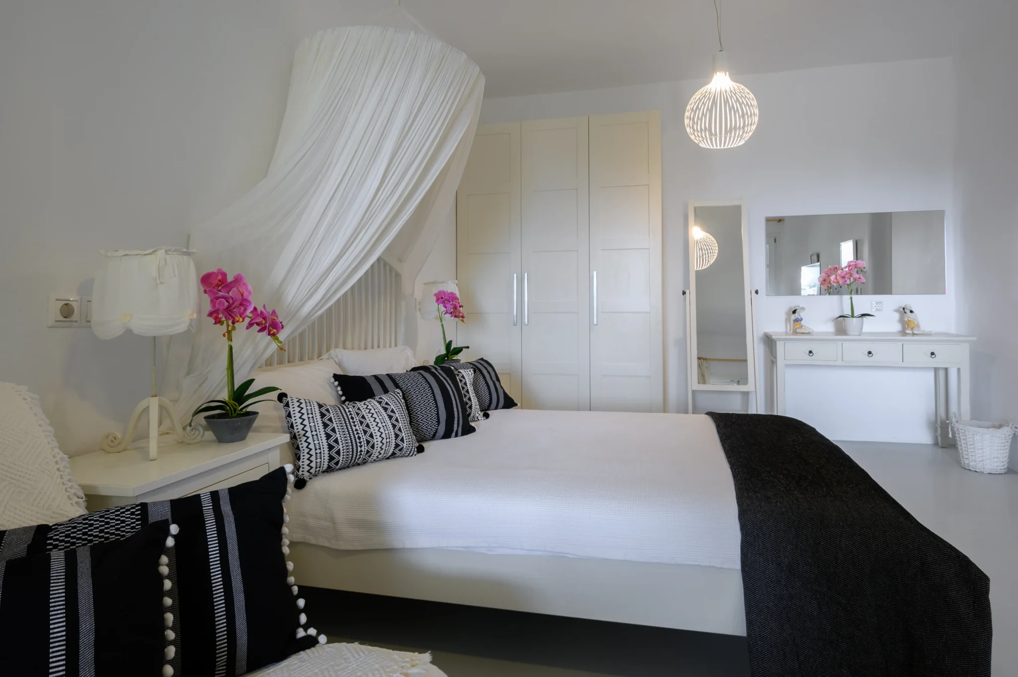 White canopy bedroom with black and white patterned cushions, pink orchids and white wardrobes at Villa Mustique in Mykonos.
