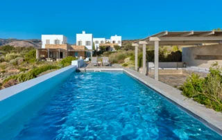 Blue swimming pool beside white and stone villa facades at Villa Olivia, Paros.