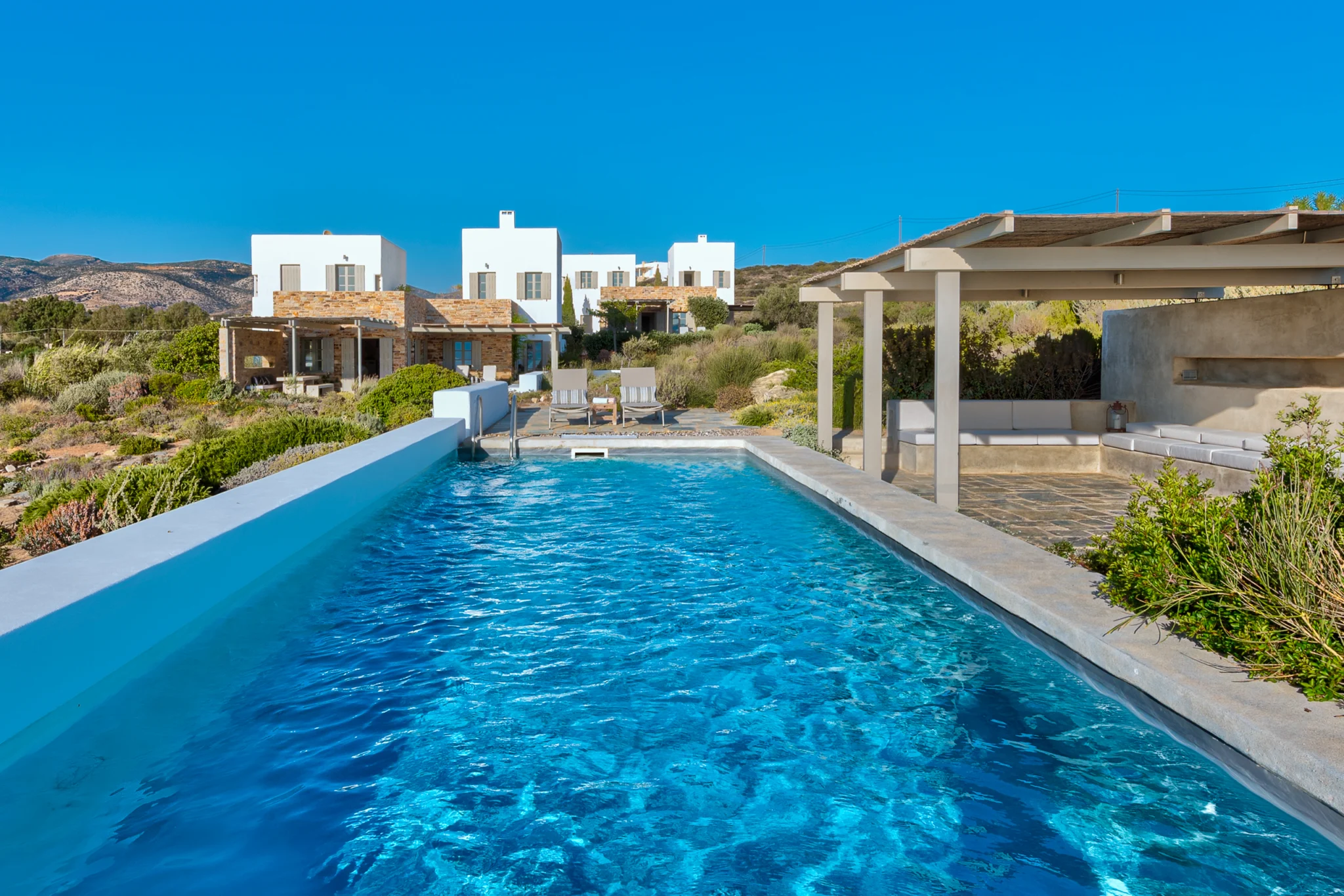 Blue swimming pool beside white and stone villa facades at Villa Olivia, Paros.