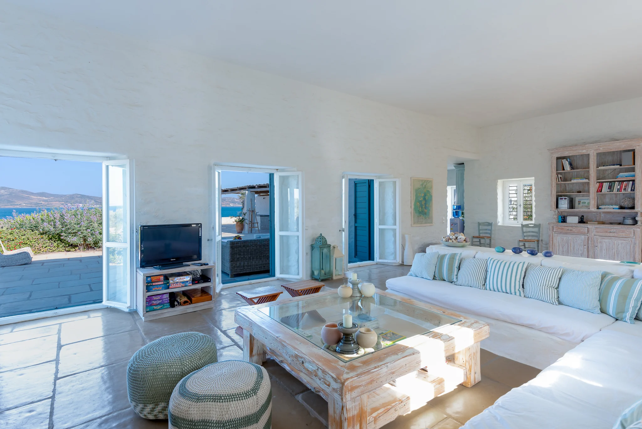 White sofa with striped cushions and turquoise doors framing the sea at Villa Salvia, Paros.