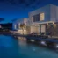 Illuminated white and stone villa reflected in the pool at blue hour at Villa Seafront, Paros.