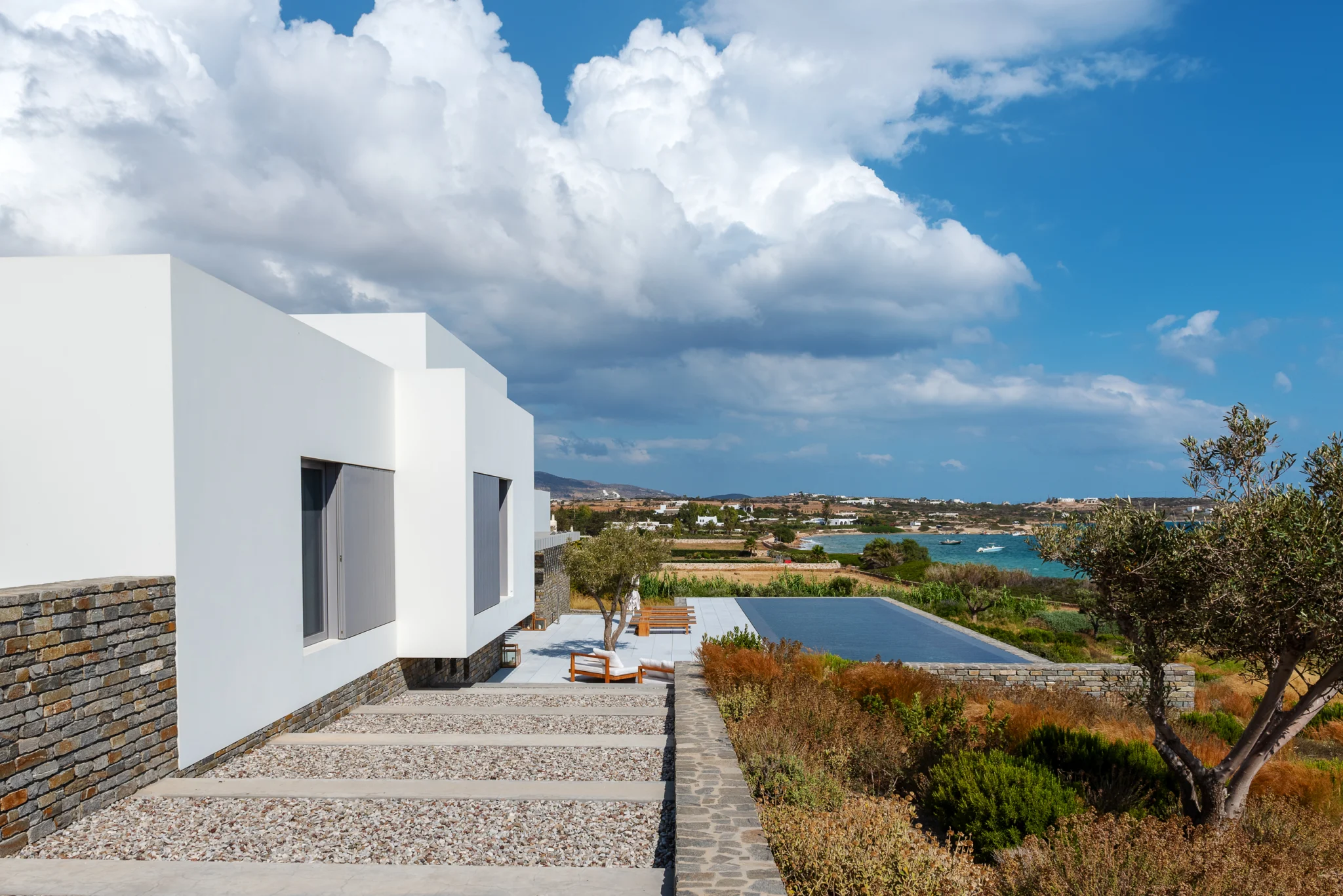 Stepping-stone path beside a white villa leading towards the pool and sea at Villa Seafront, Paros.