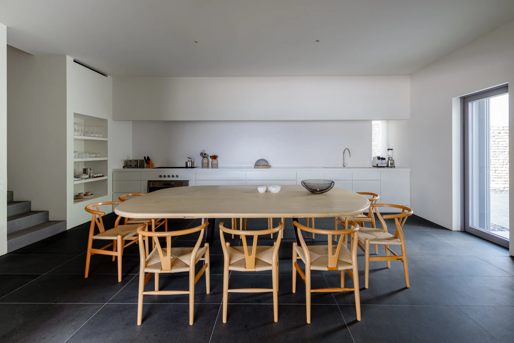 Timber dining table and curved chairs beside a minimal white kitchen at Villa Seafront, Paros.