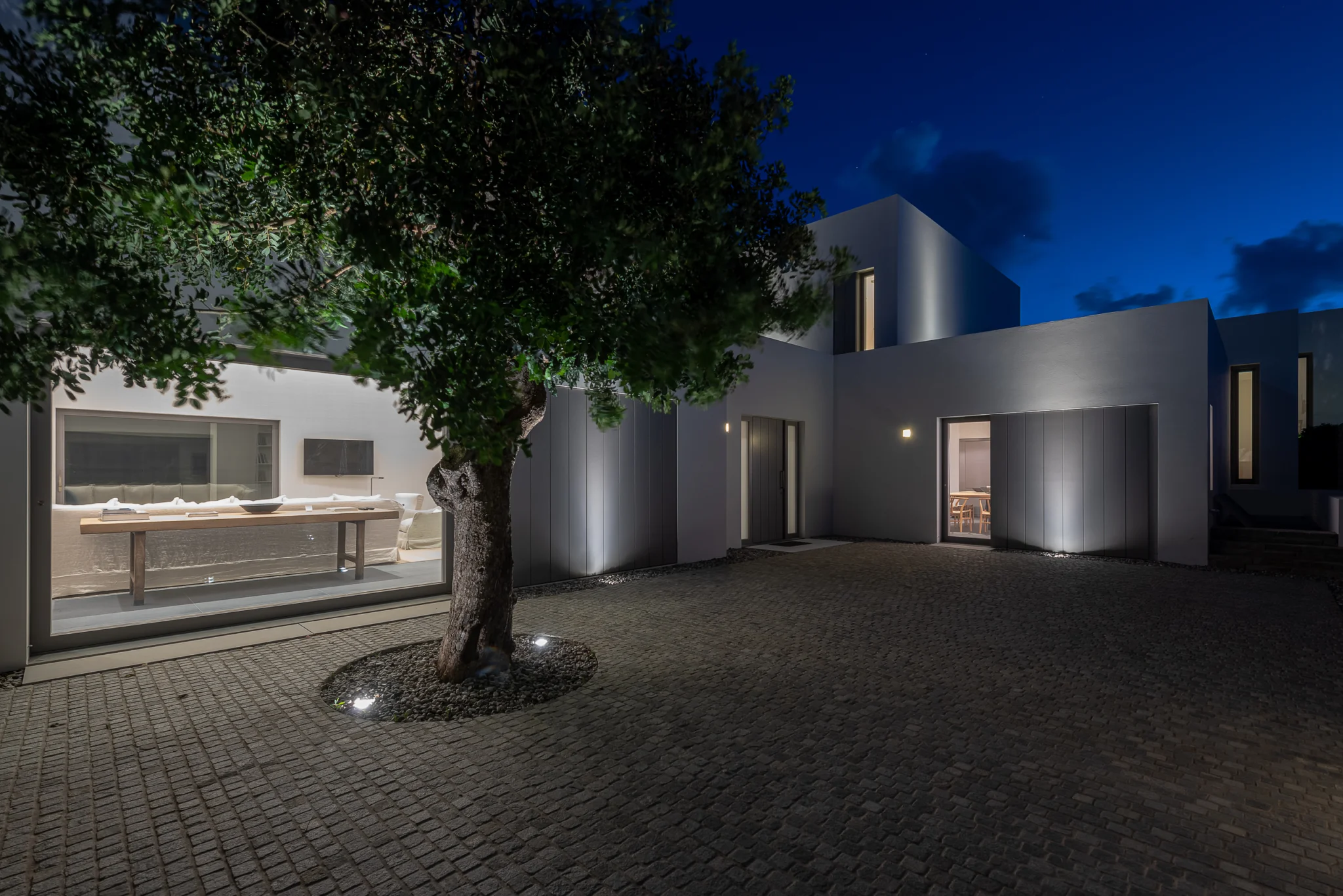 Illuminated entrance courtyard beneath an olive tree at night at Villa Seafront, Paros.